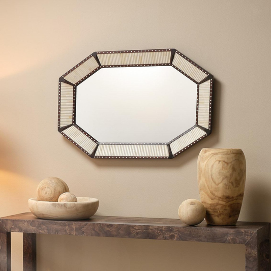 Octagonal mirror on a beige wall with decorative items on a wooden console table.