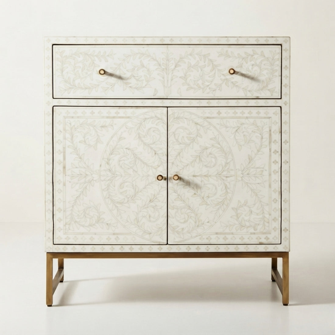 A cream-colored console cabinet with intricate shell-like floral patterns and brass legs, styled in a modern, warm-toned living room setting.
