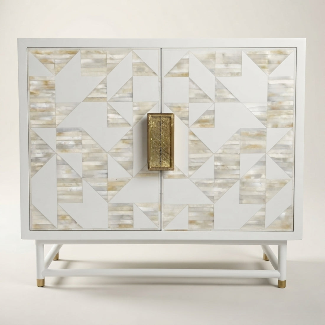 A white two-door cabinet with geometric shell-patterned doors and a central brass handle, styled in a modern living room next to a beige sofa.