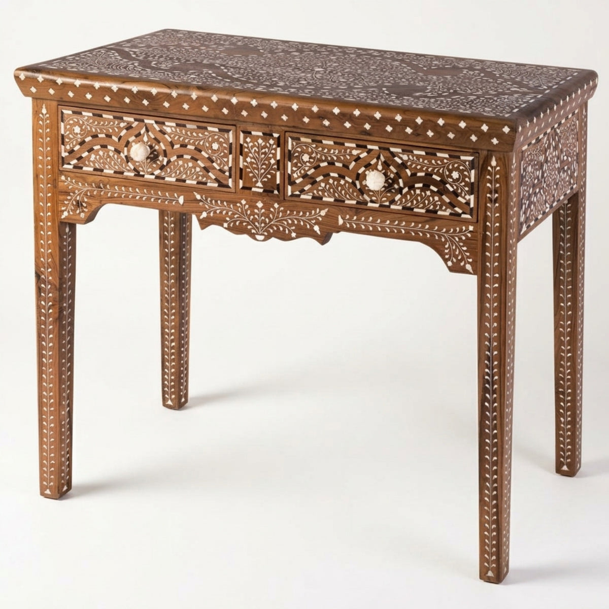 An ornate wooden writing desk with intricate bone or mother-of-pearl inlay detailing, featuring two drawers with carved floral fronts and decorative legs, shown on a light gray background.