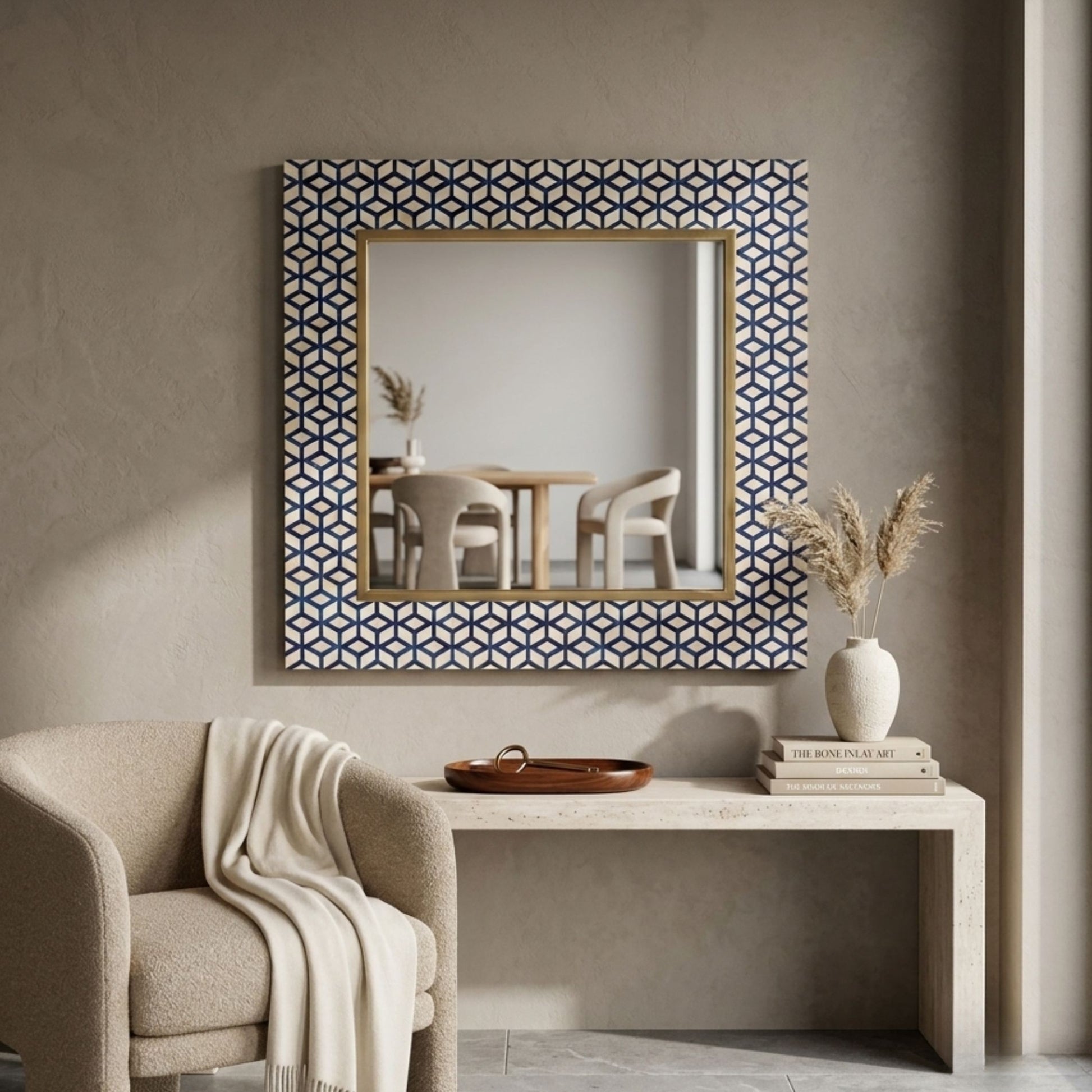 A square wall mirror with a geometric blue and white patterned frame and a gold inner border, displayed in a styled interior setting above a console table.