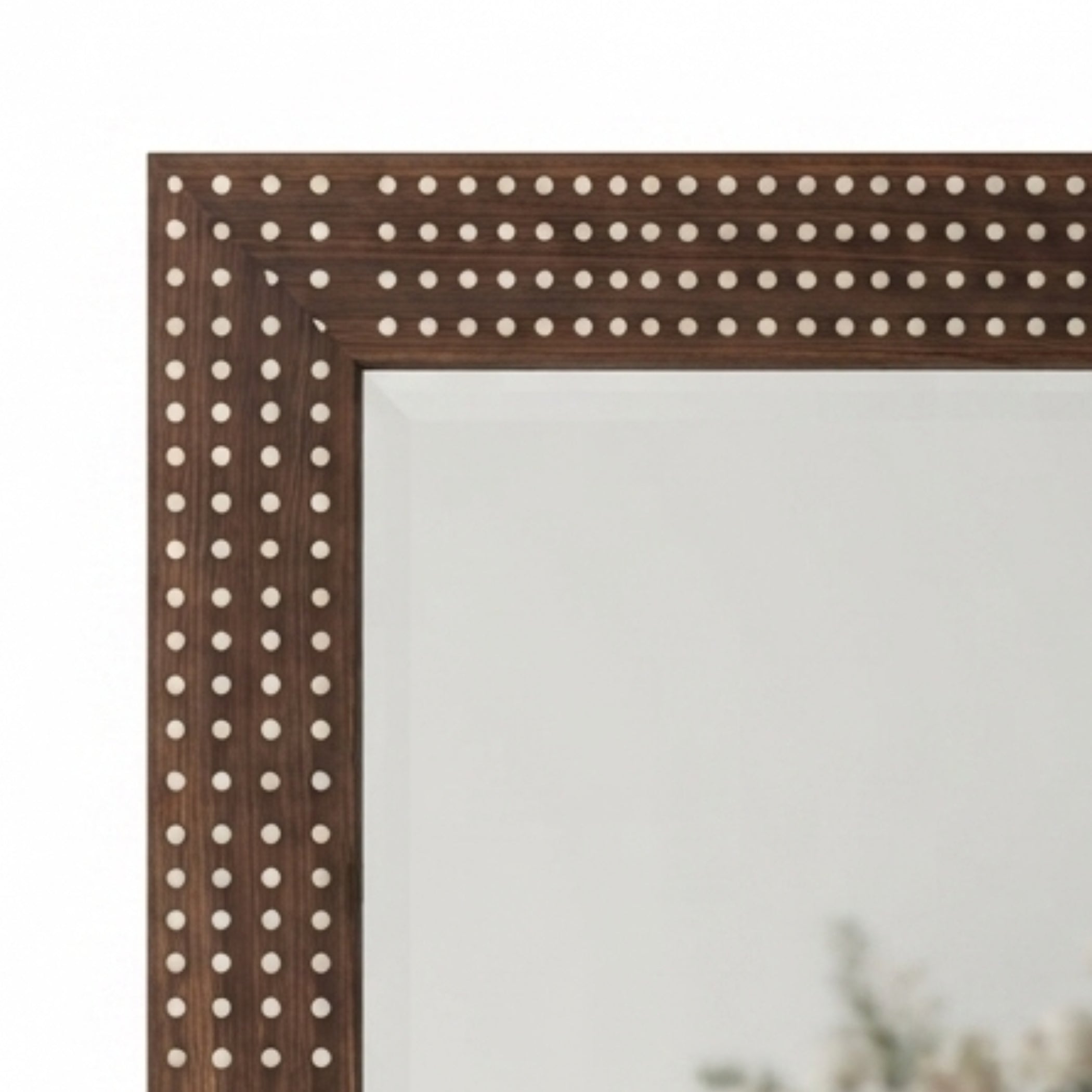 Close-up of a dark brown wooden mirror frame decorated with rows of small round metallic studs, shown against a white background.