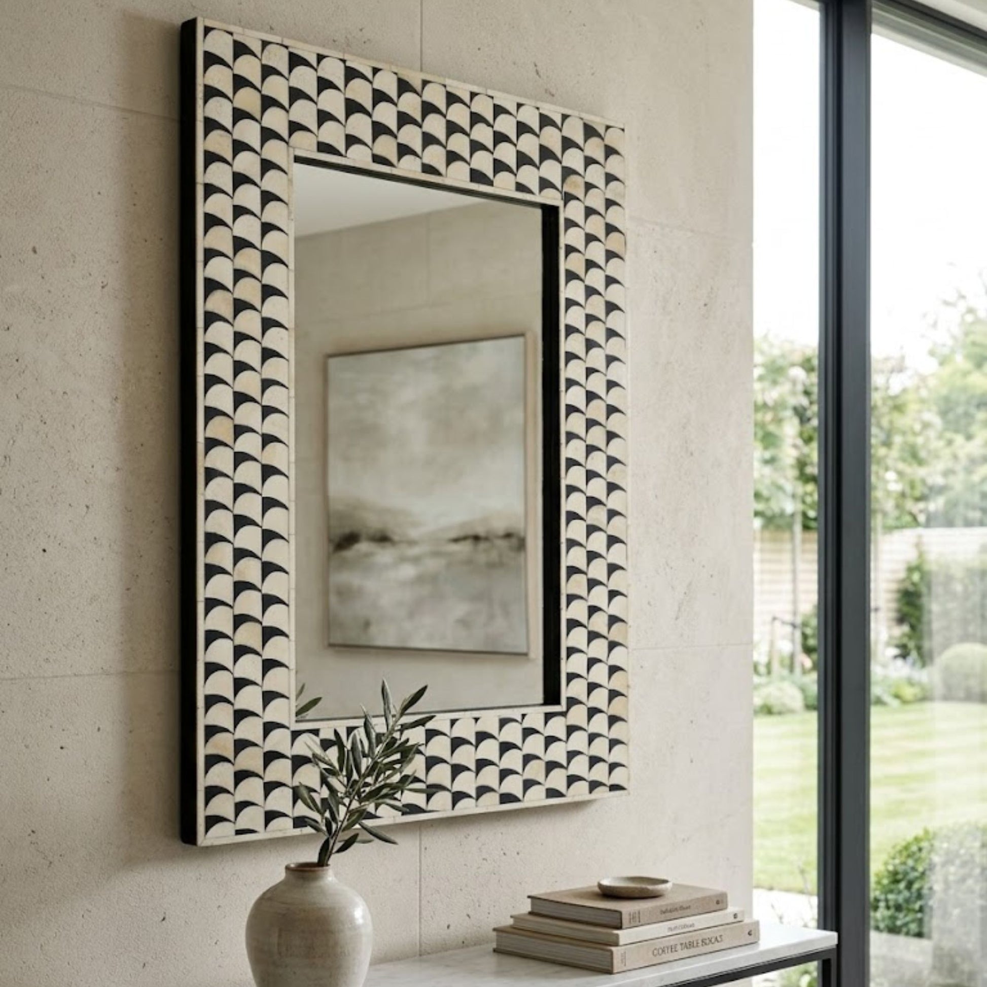 A rectangular wall mirror with a black and white scalloped fan-pattern frame, mounted on a light beige stone wall in a modern interior setting.