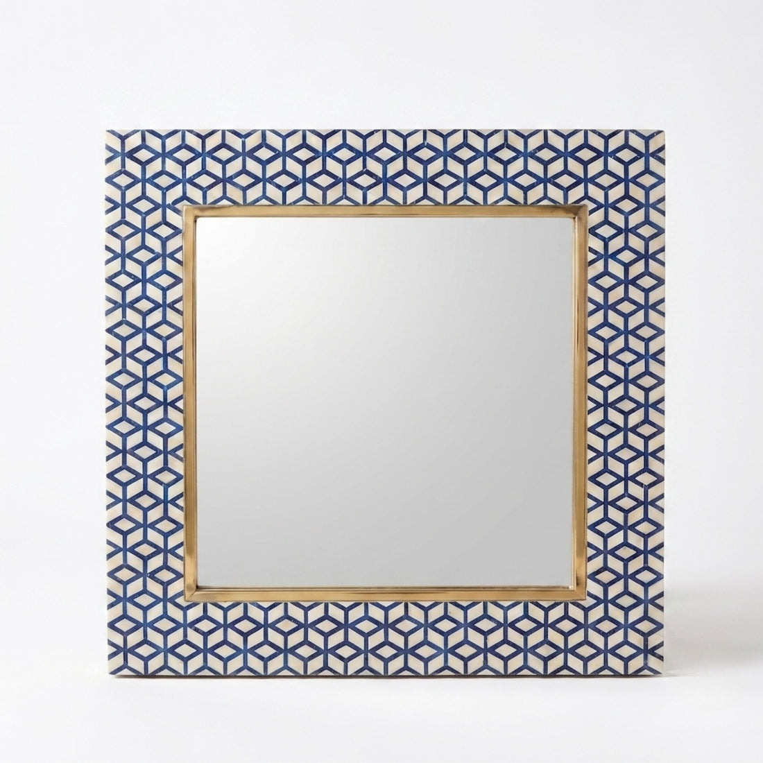 A square wall mirror with a geometric blue and white patterned frame and a gold inner border, displayed in a styled interior setting above a console table.