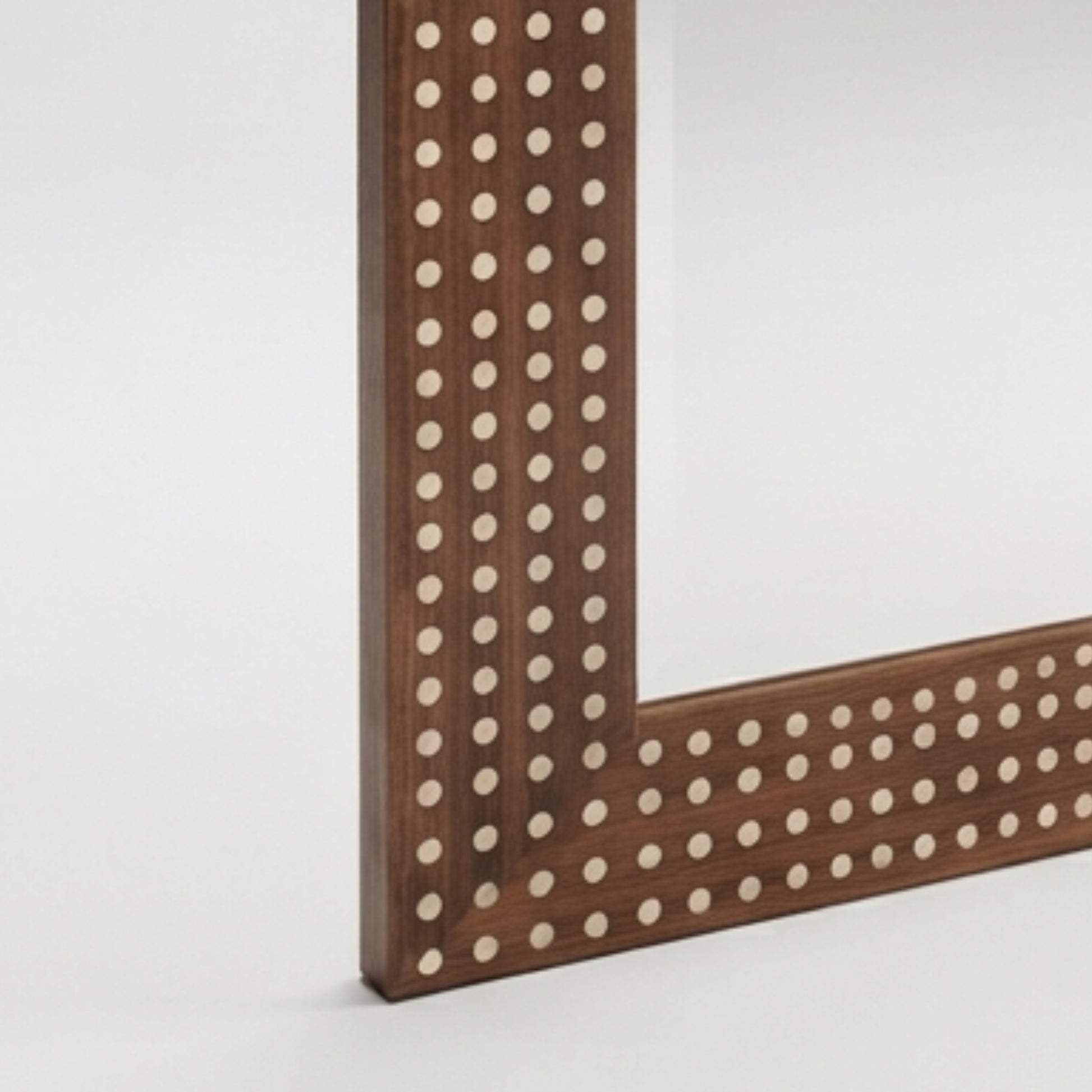 Close-up of a wooden mirror frame corner with evenly spaced round inlay dots on a light gray background.