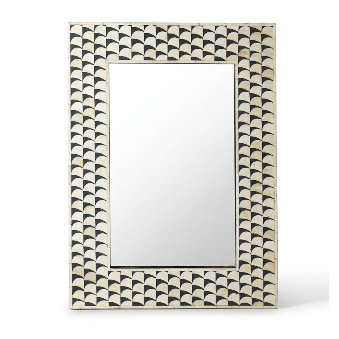 A rectangular wall mirror with an intricate black and beige scalloped geometric frame, styled on a light stone pedestal in a warm, neutral-toned room.