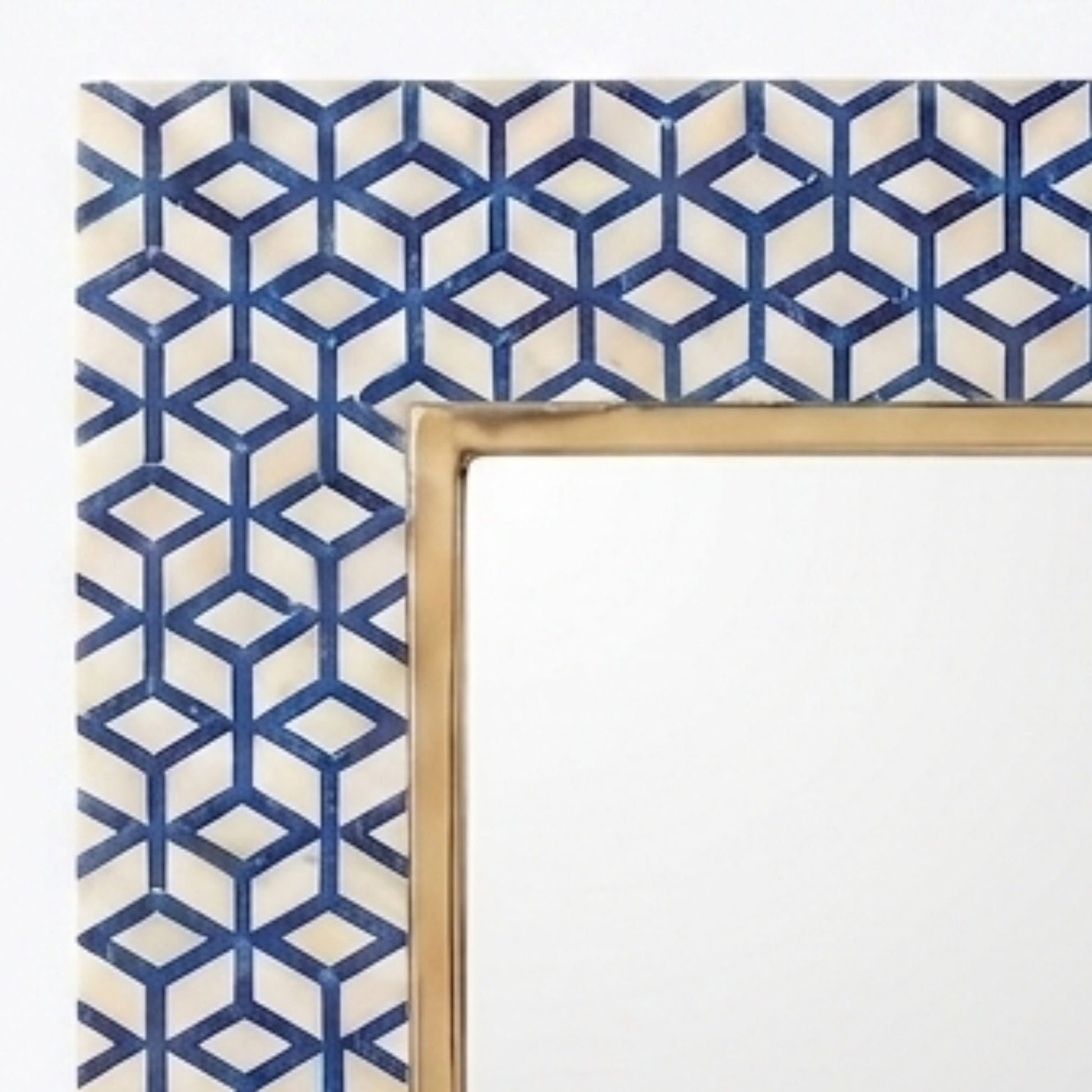 A close-up of a decorative mirror frame corner featuring a blue and cream geometric cube pattern with a gold-toned inner border.