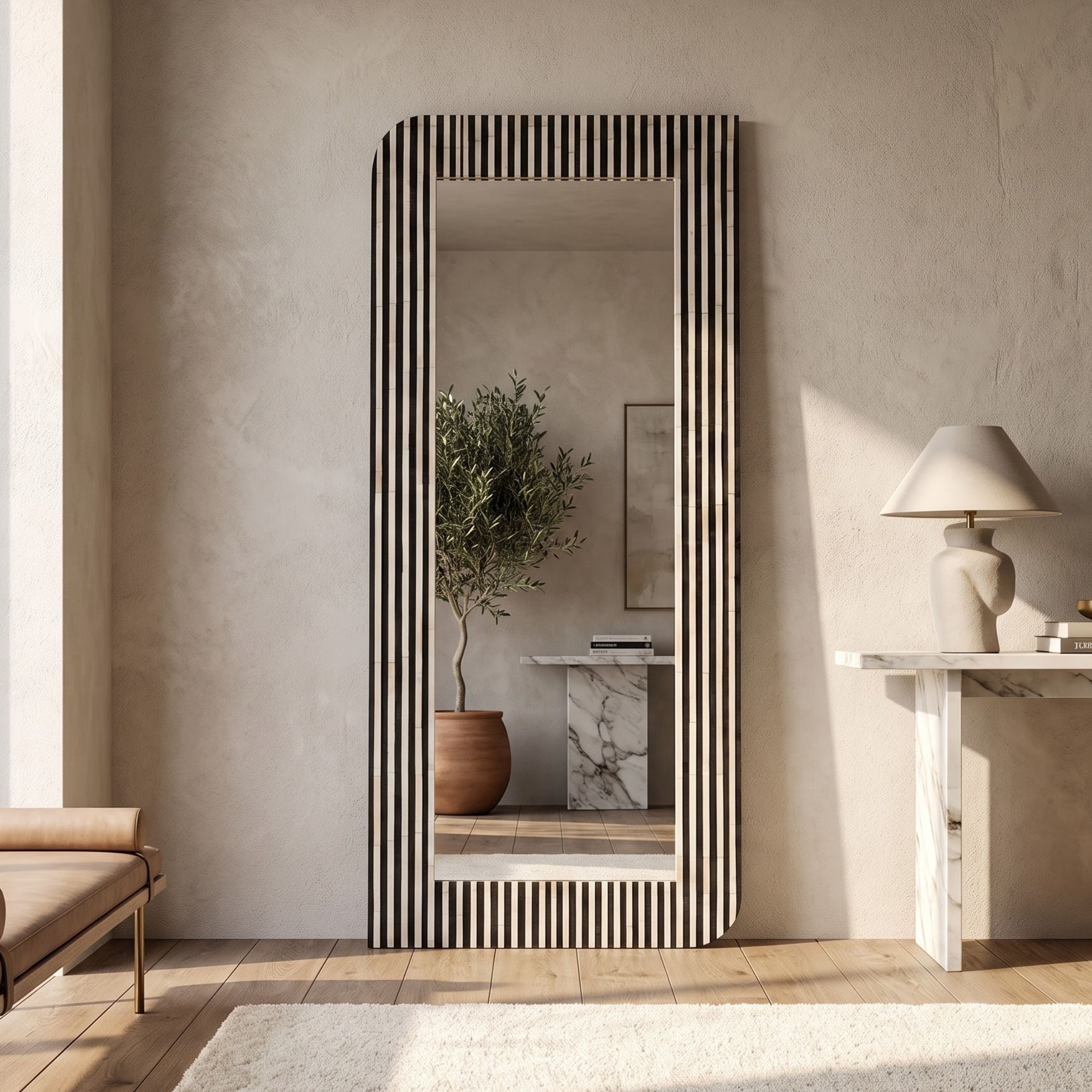 A tall rectangular floor mirror with a black and white vertically striped frame, styled in a minimalist beige-toned room with a marble console table and a potted olive tree reflected in the glass.