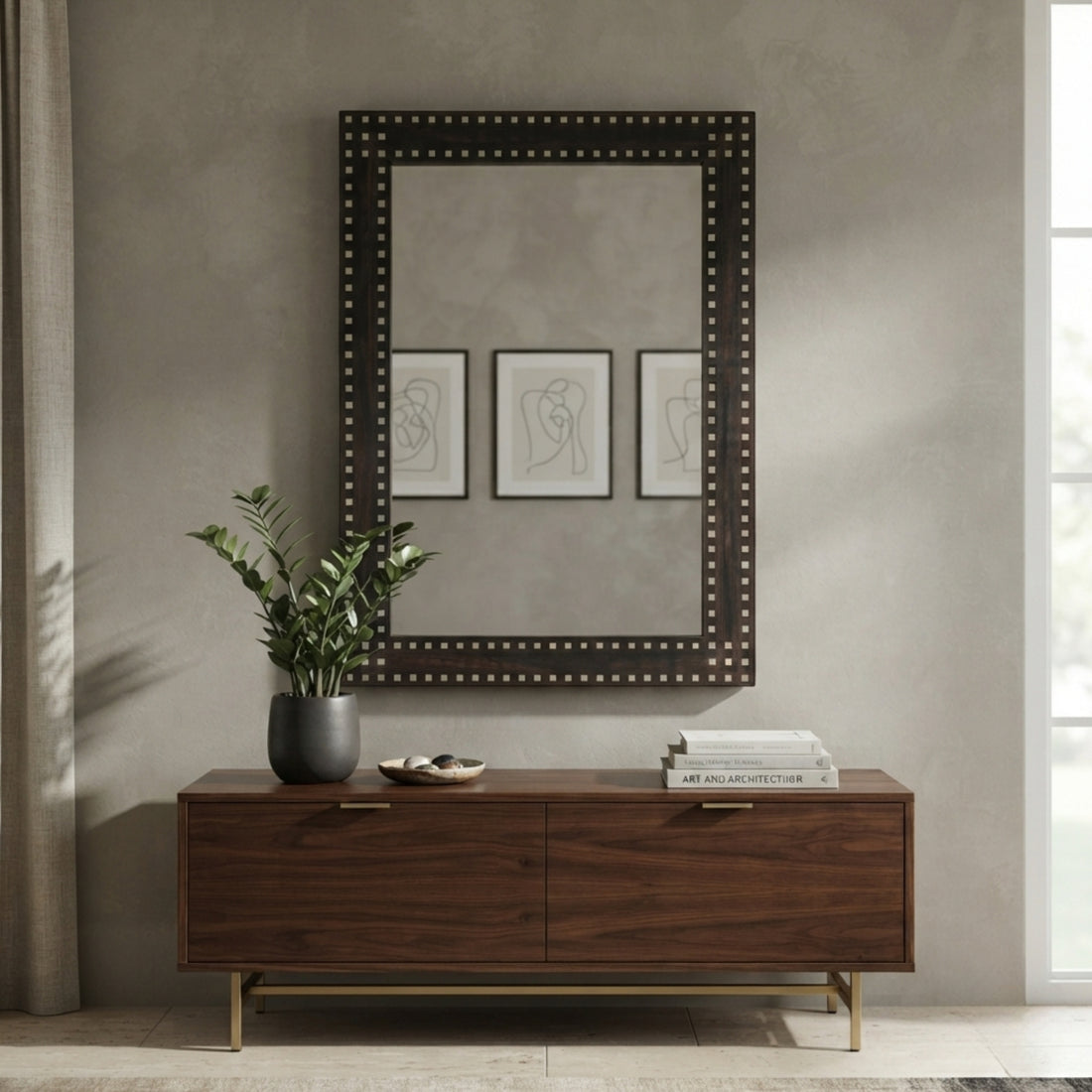 A large rectangular wall mirror with a dark wood frame and silver nailhead trim hangs above a dark wood console table in a styled interior setting.