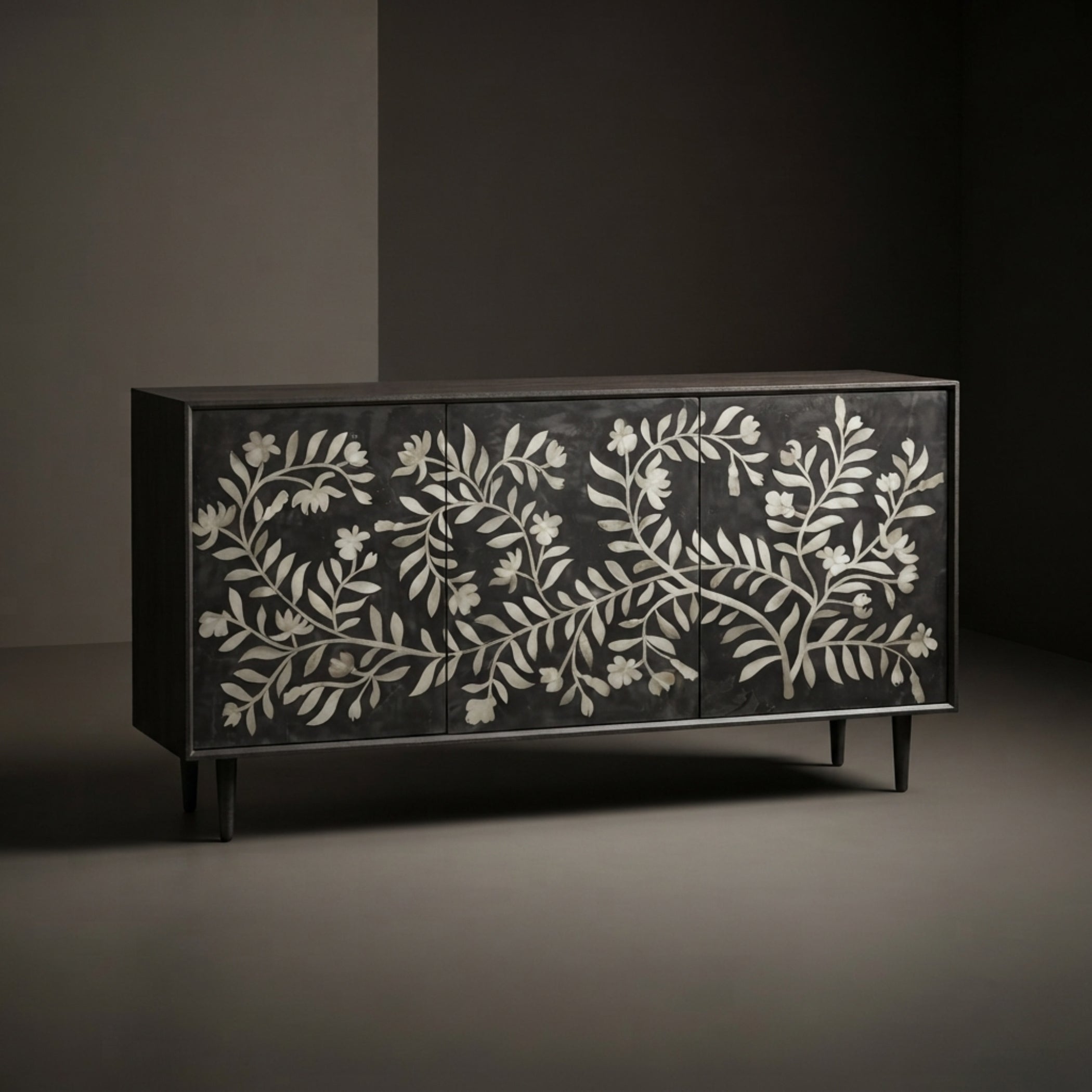 A black wooden sideboard with intricate white bone or shell floral inlay across the front, set against a dark gray studio background.