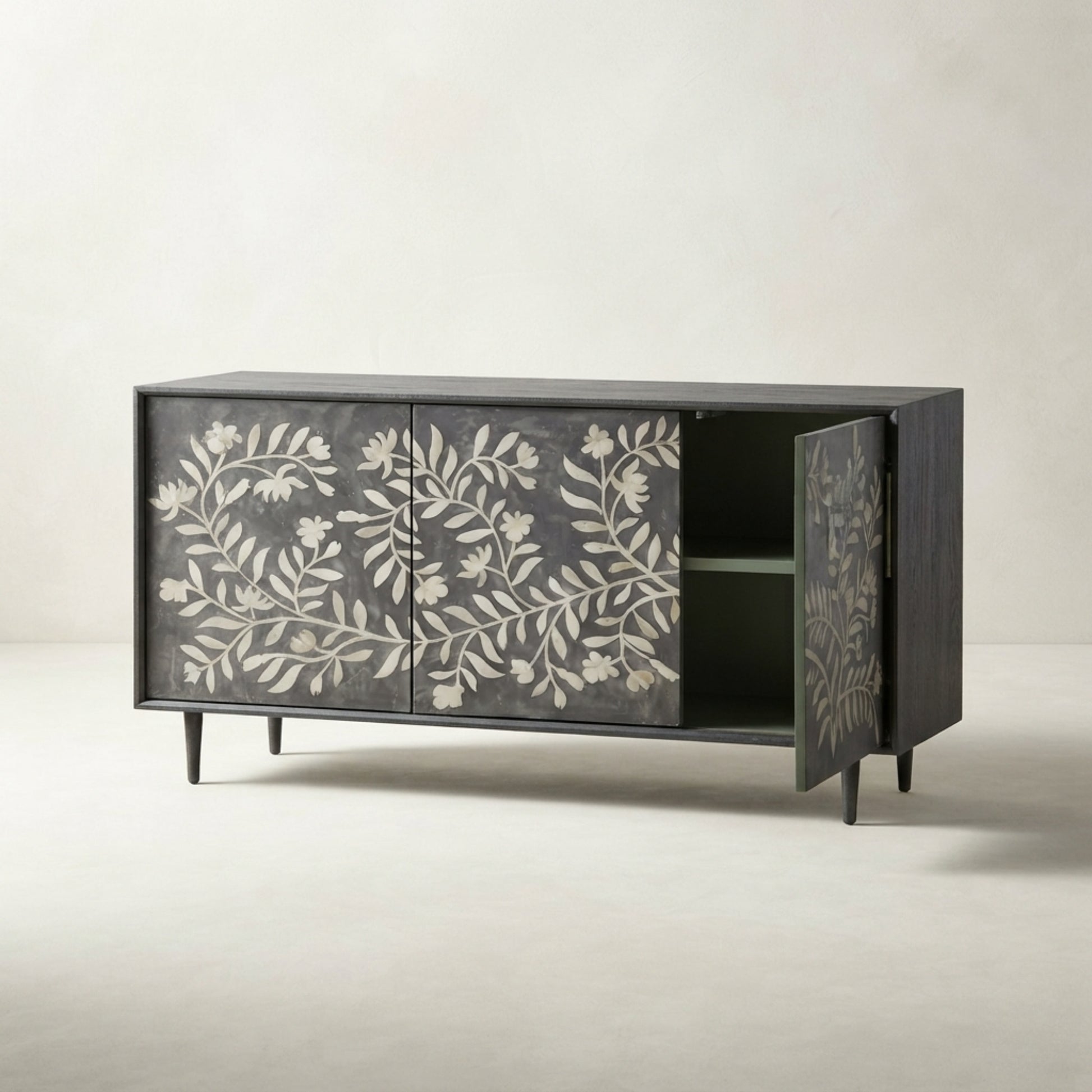 A mid-century modern sideboard cabinet with a dark charcoal gray wood finish and white floral inlay on the doors, shown with one door open to reveal a green interior shelf.