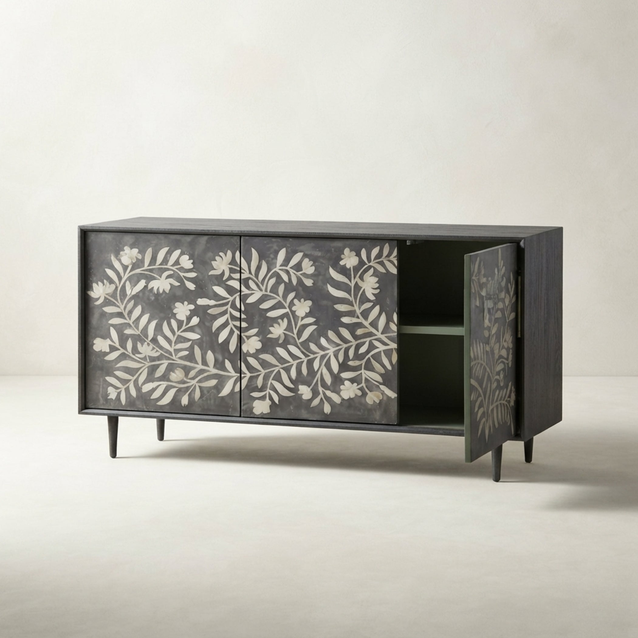 A mid-century modern sideboard cabinet with a dark charcoal gray wood finish and white floral inlay on the doors, shown with one door open to reveal a green interior shelf.