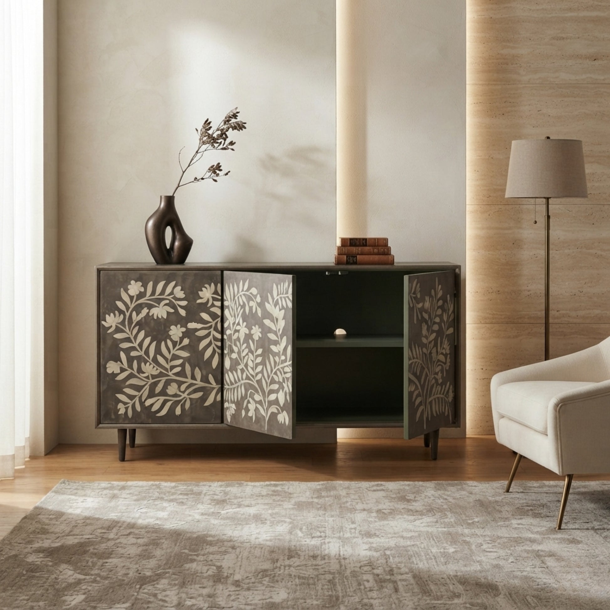 A mid-century modern sideboard cabinet with dark gray doors featuring a beige botanical leaf pattern, styled in a warm, neutral-toned living room next to a white armchair and a floor lamp.