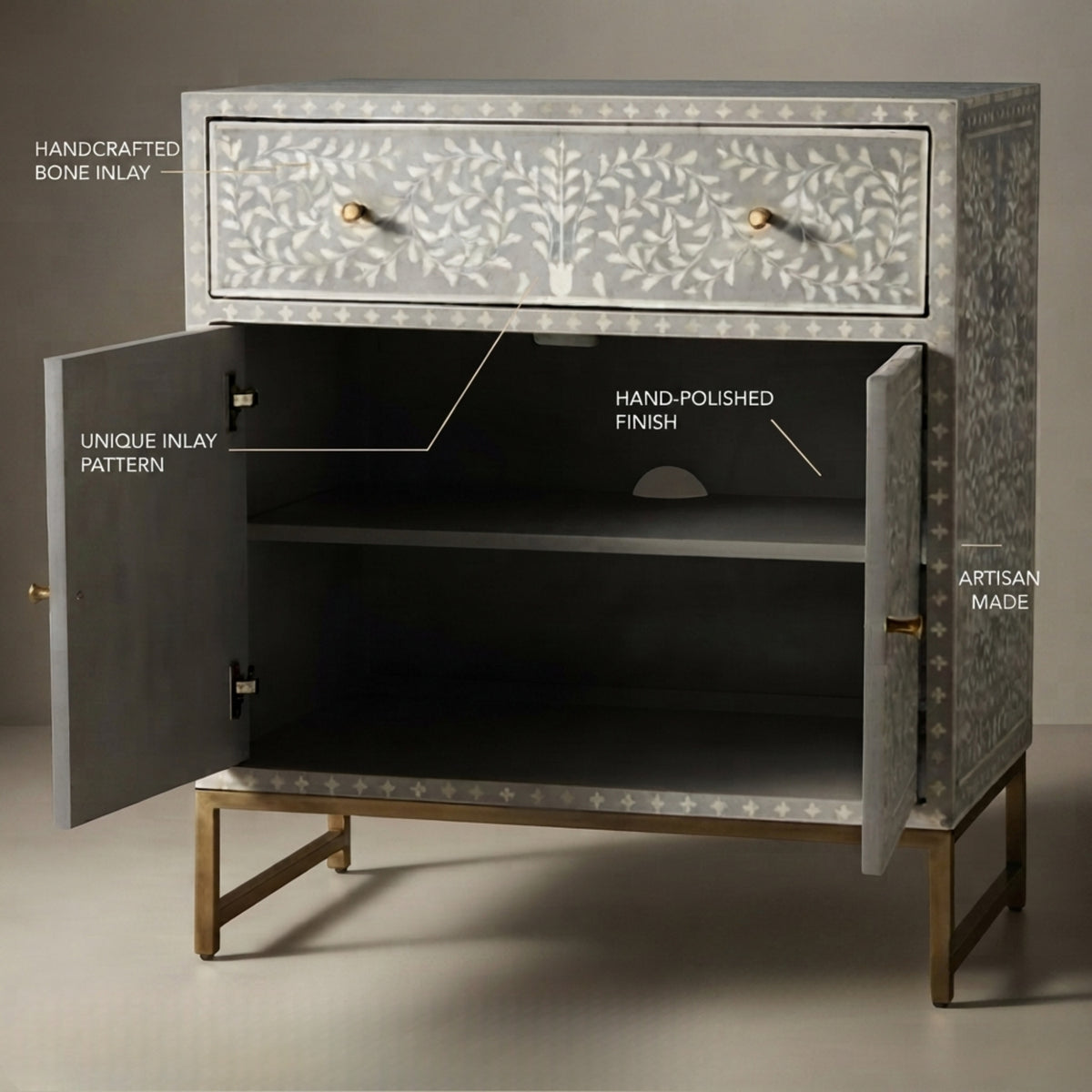 A handcrafted two-drawer cabinet with open doors, featuring a light gray bone-inlay pattern with leaf motifs, gold-tone knobs, and brass legs. White text labels point out key features like handcrafted bone inlay, unique inlay pattern, hand-polished finish, and artisan made, set against a neutral studio background.