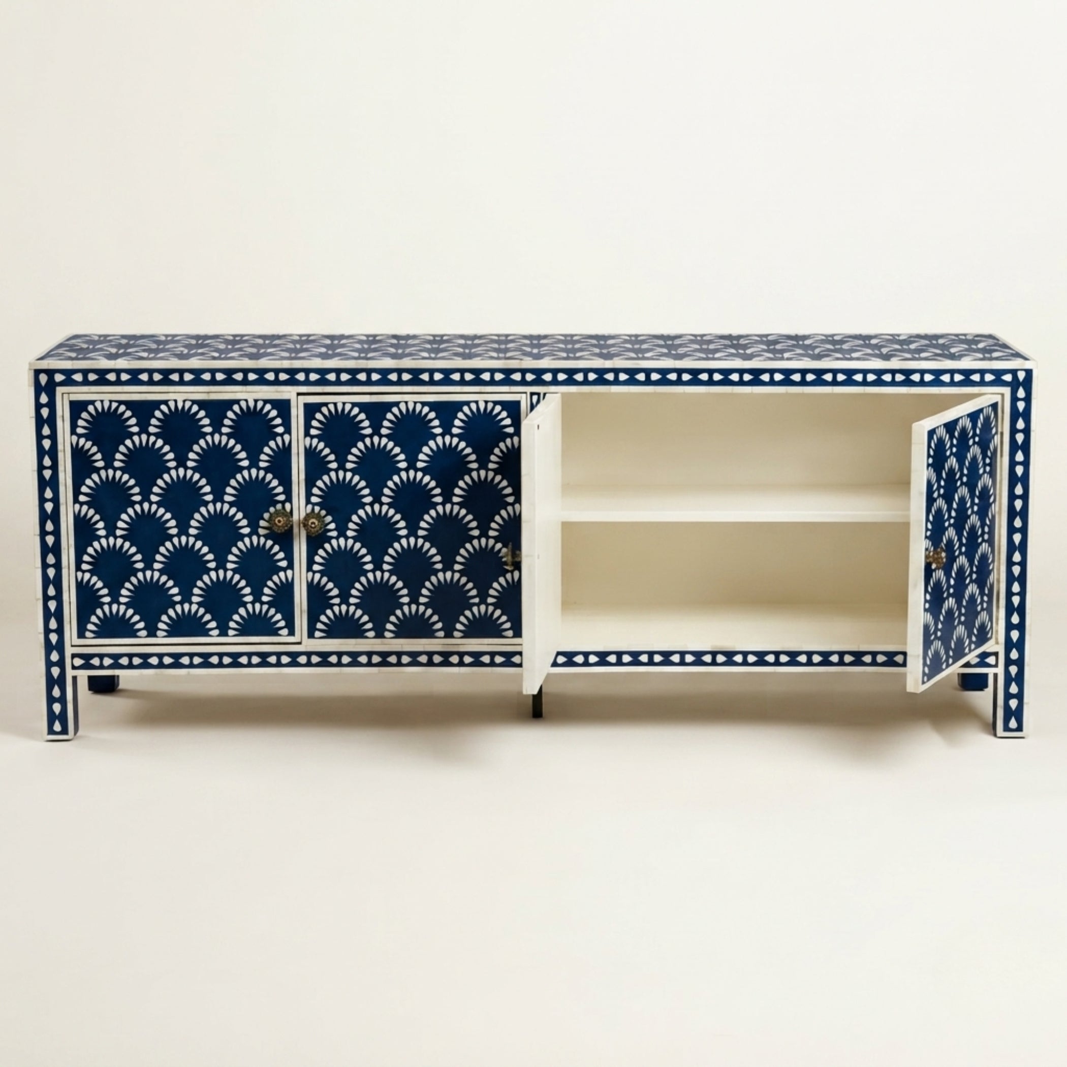 A white sideboard cabinet with intricate navy blue and white hand-painted fan and dot patterns, featuring two doors and an open center shelf.
