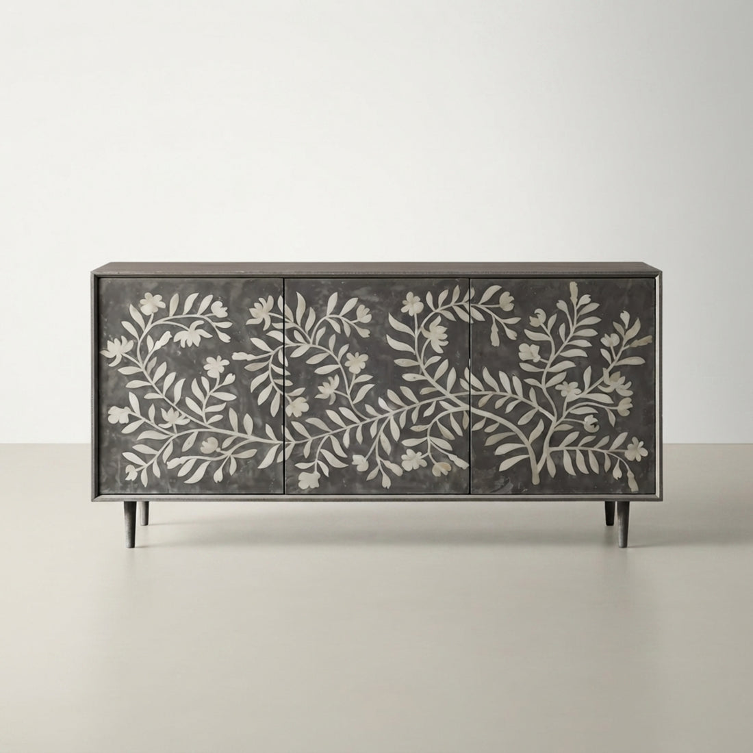 A dark gray sideboard cabinet with a white floral branch pattern on the front, styled in a modern interior with a vase and books on top.