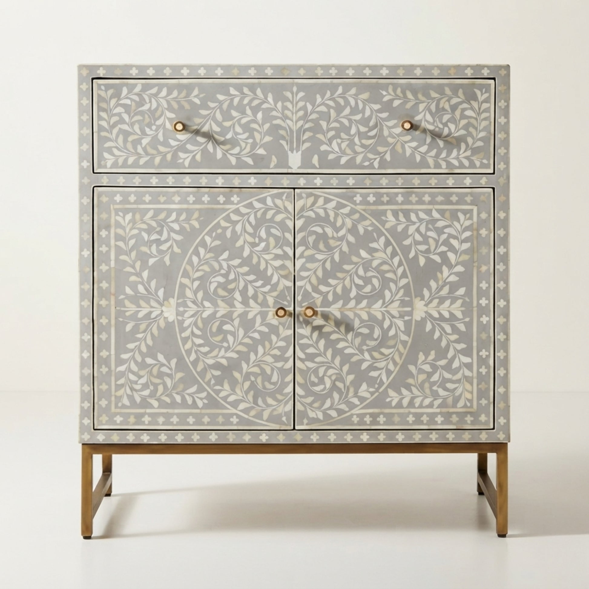 A light gray bone-inlay sideboard cabinet with white floral patterns, gold-tone legs, and small round gold knobs, shown against a plain off-white background.