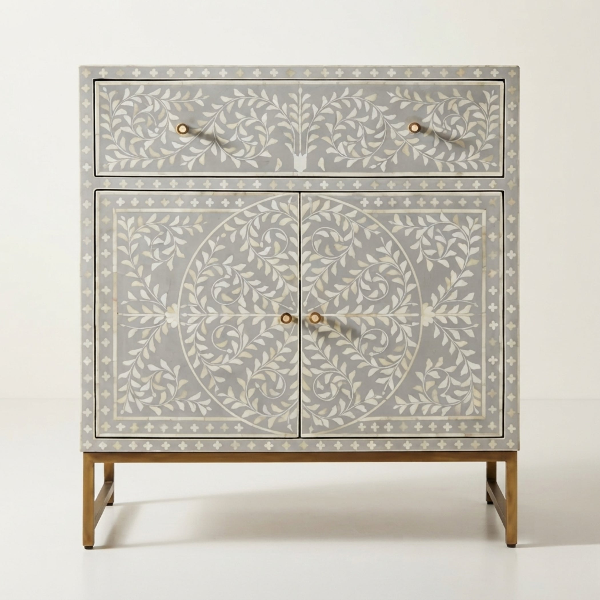 A light gray bone-inlay sideboard cabinet with white floral patterns, gold-tone legs, and small round gold knobs, shown against a plain off-white background.