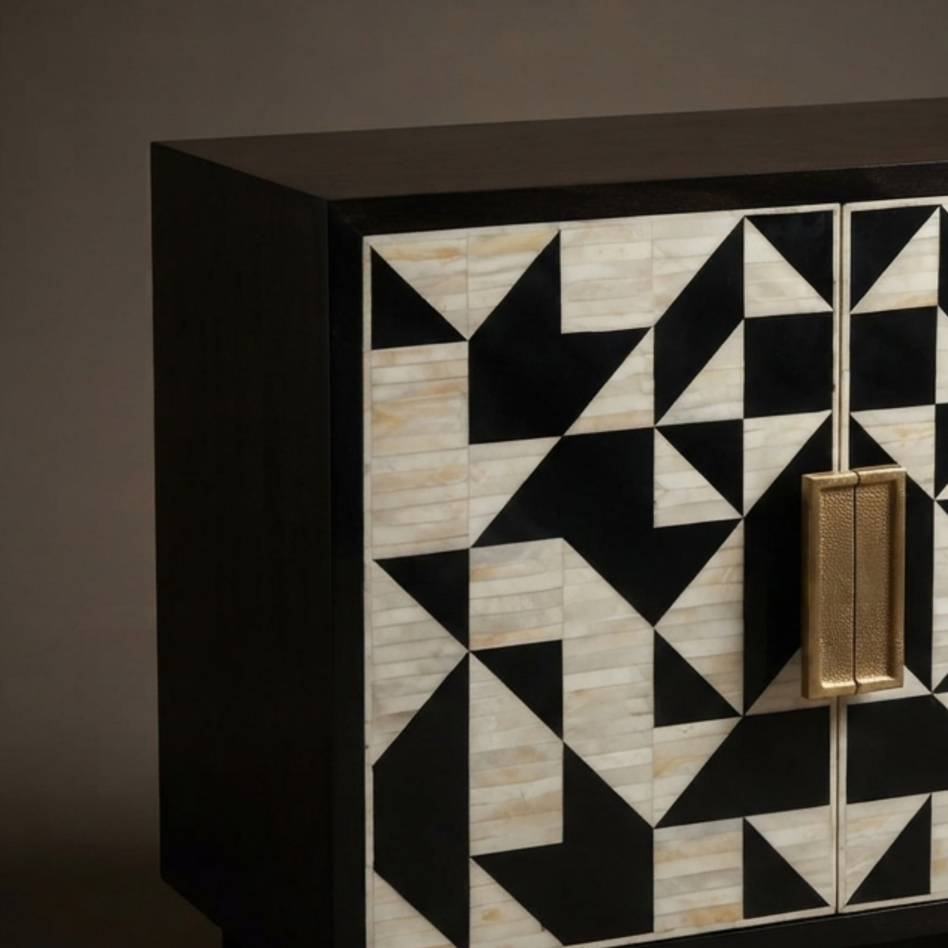 A close-up of a modern sideboard or cabinet with a black frame and geometric inlay pattern on the doors, featuring alternating black and light beige stone-like triangles, with a vertical gold handle.