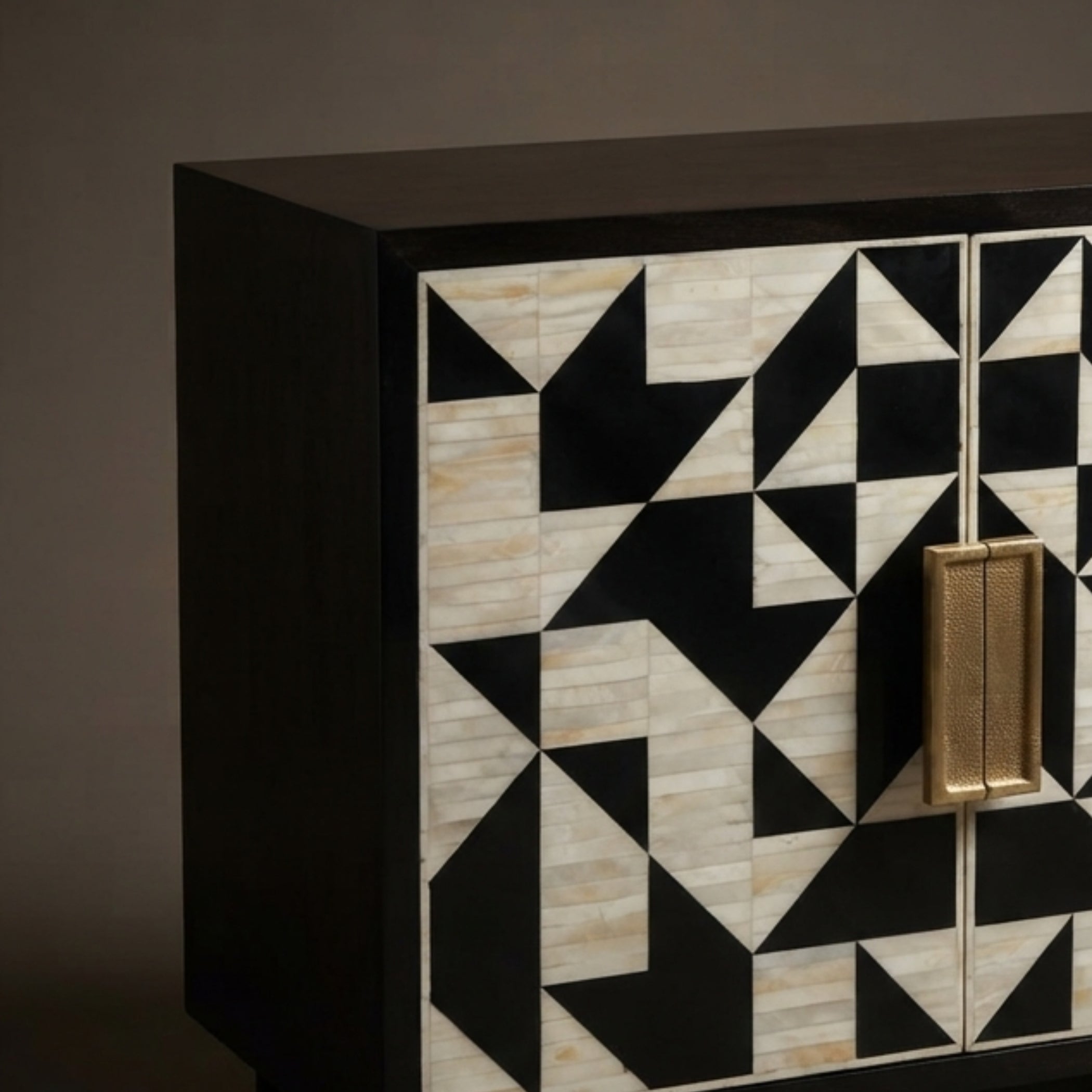 A close-up of a modern sideboard or cabinet with a black frame and geometric inlay pattern on the doors, featuring alternating black and light beige stone-like triangles, with a vertical gold handle.