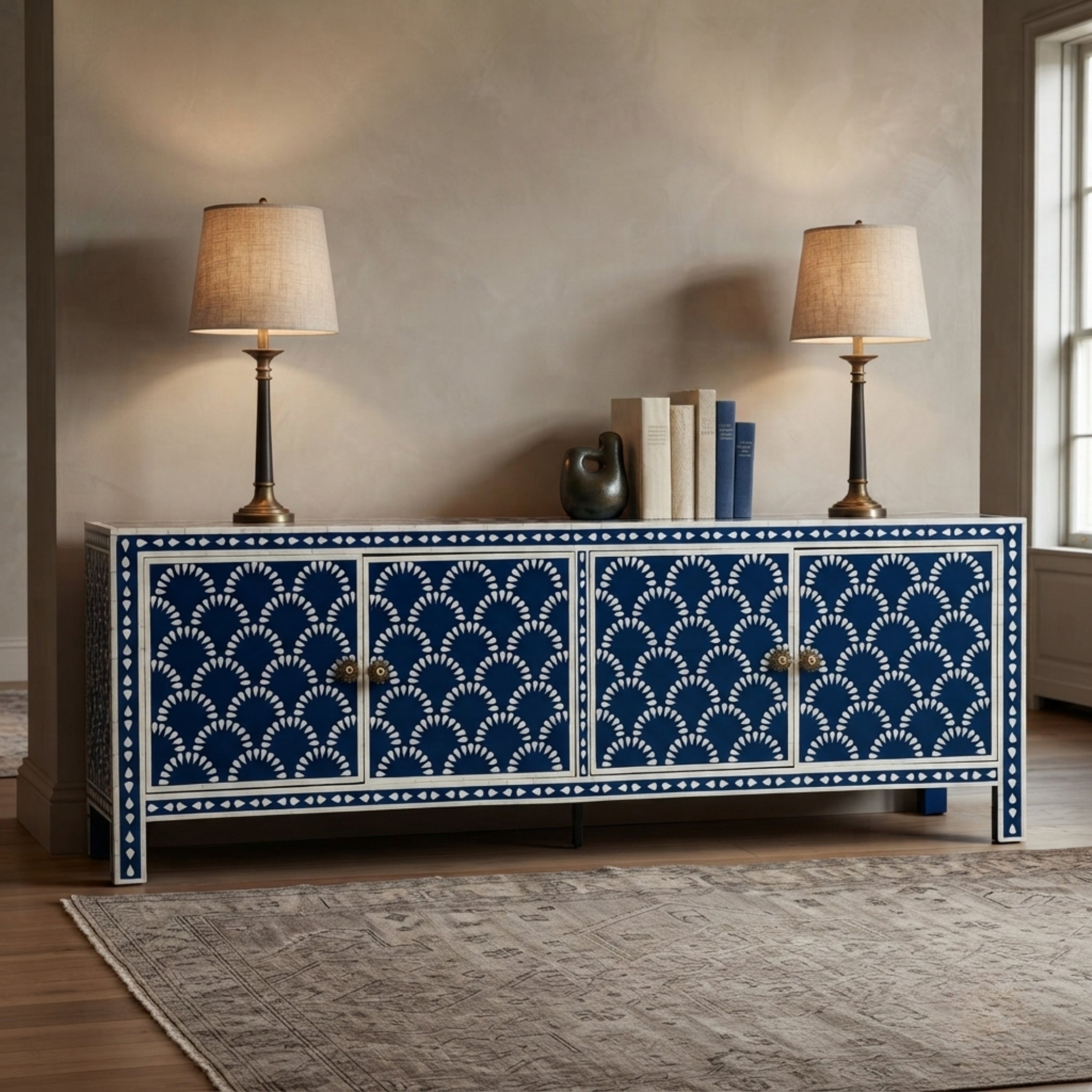 A blue and white patterned sideboard cabinet in a styled room, topped with two table lamps and books, set against a neutral beige wall.