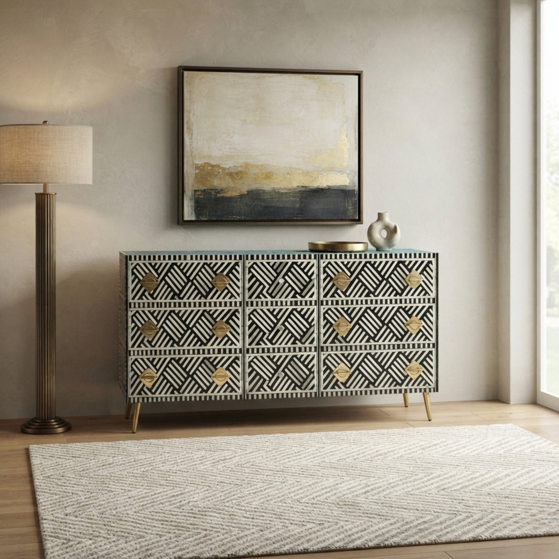 A bone-and-wood sideboard cabinet with a black and white geometric pattern and gold drawer pulls, styled in a modern living room setting with a floor lamp, framed art, and a rug.