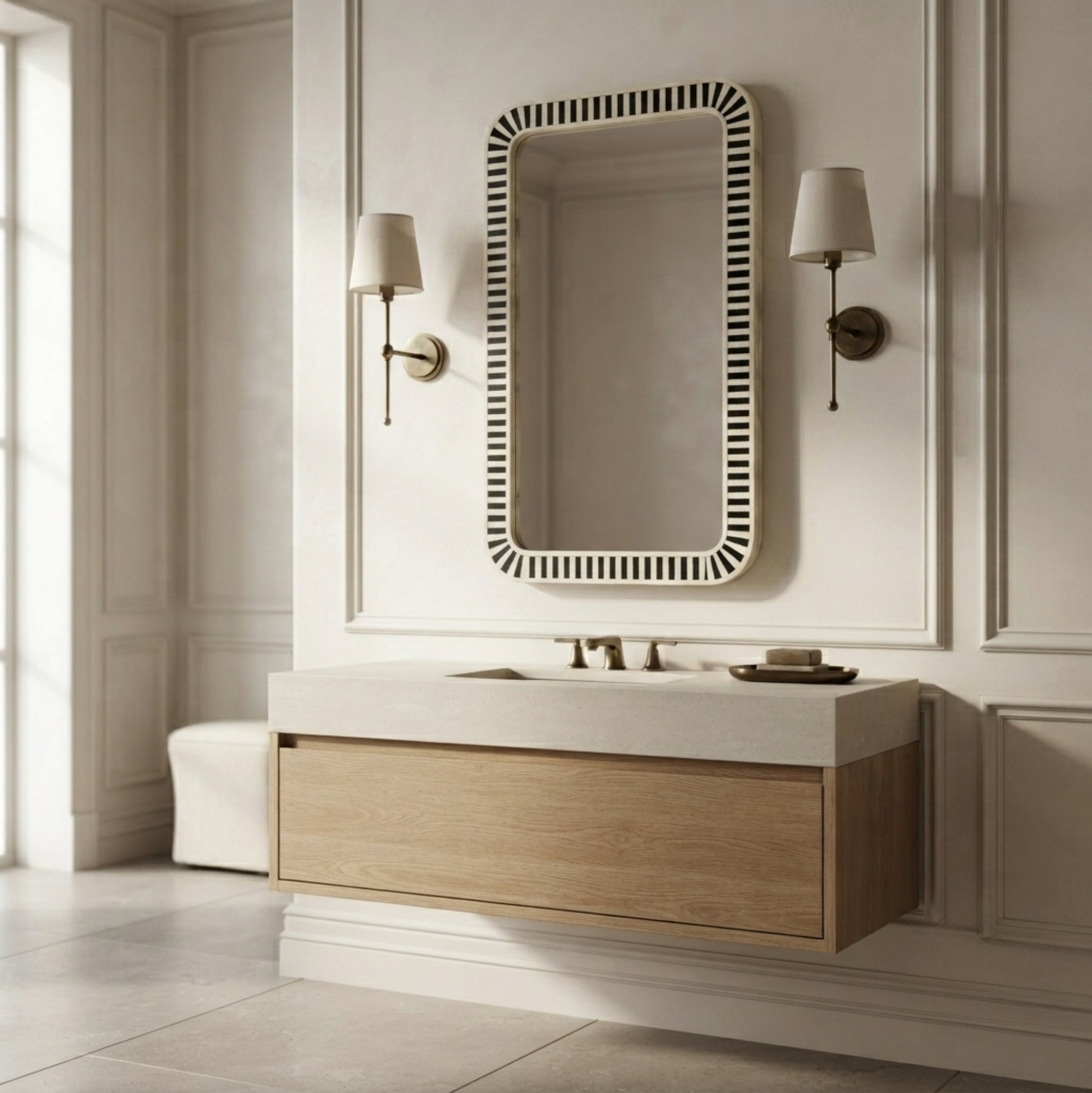 A modern wall-mounted bathroom vanity with a light wood cabinet, white countertop, and integrated sink, styled in a bright, elegant room with a black-and-white striped rectangular mirror and wall sconces.