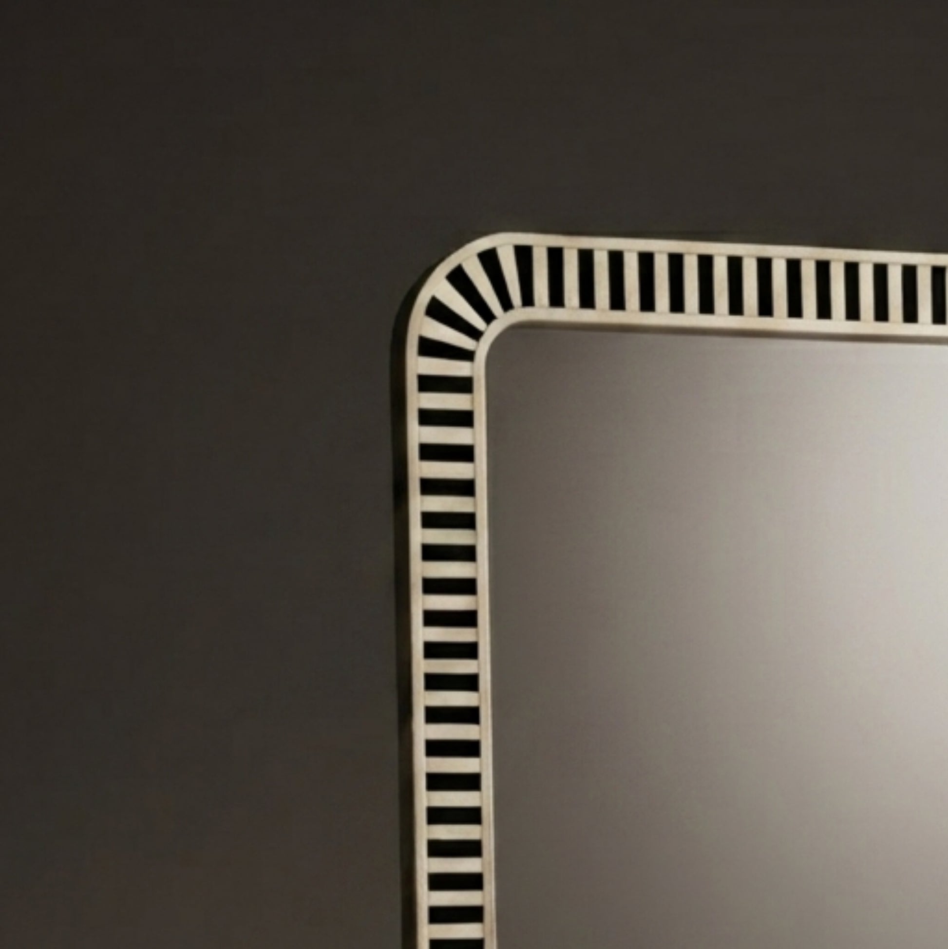 A close-up of a rectangular wall mirror with a white frame featuring a black-and-white striped border design, set against a dark gray wall.