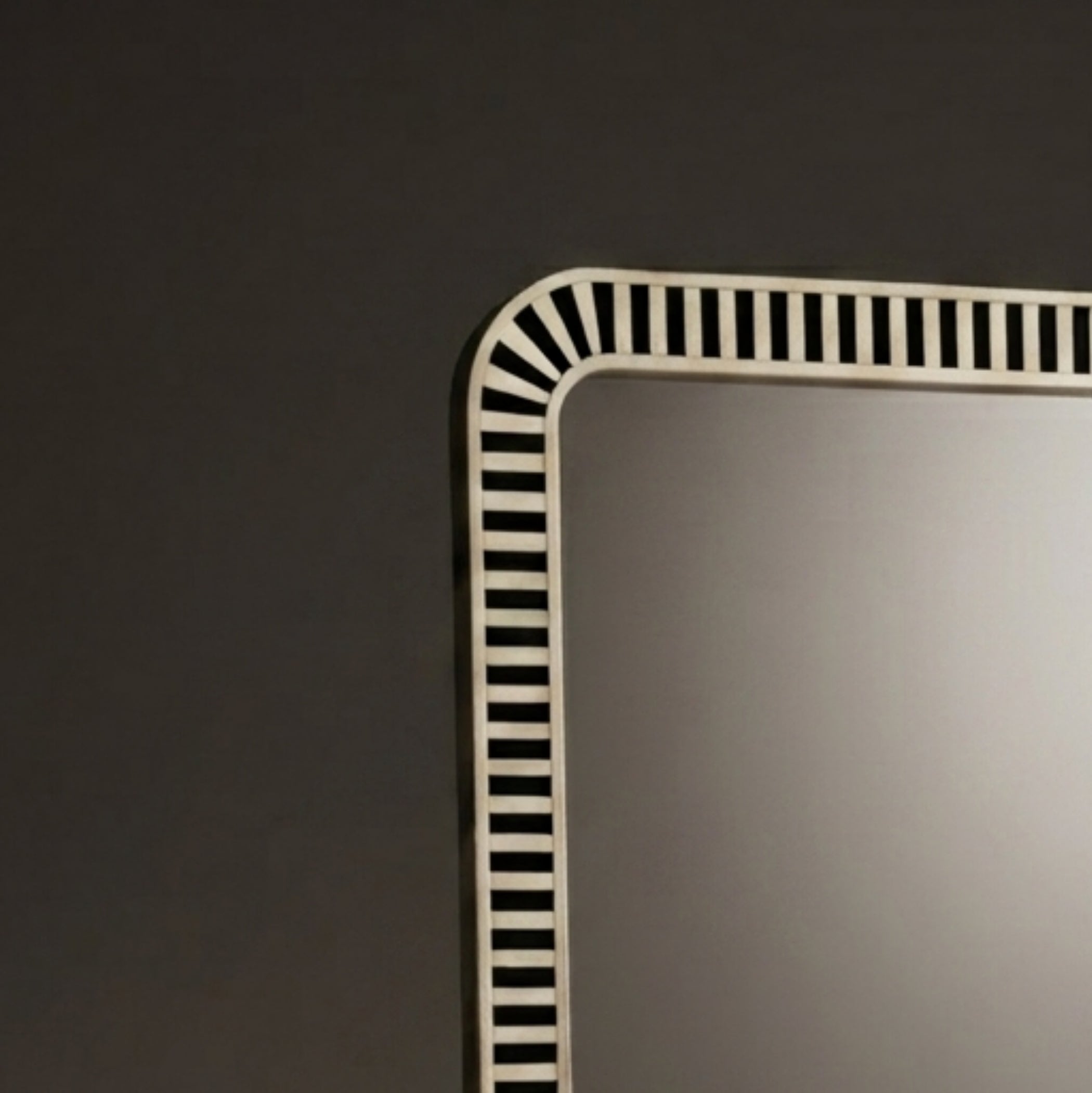 A close-up of a rectangular wall mirror with a white frame featuring a black-and-white striped border design, set against a dark gray wall.