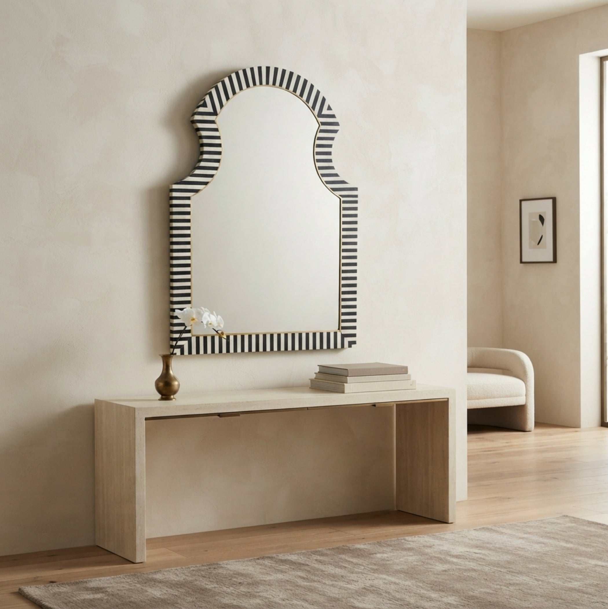 Arched wall mirror with a black and white striped border, mounted above a light wood console table in a neutral-toned room.