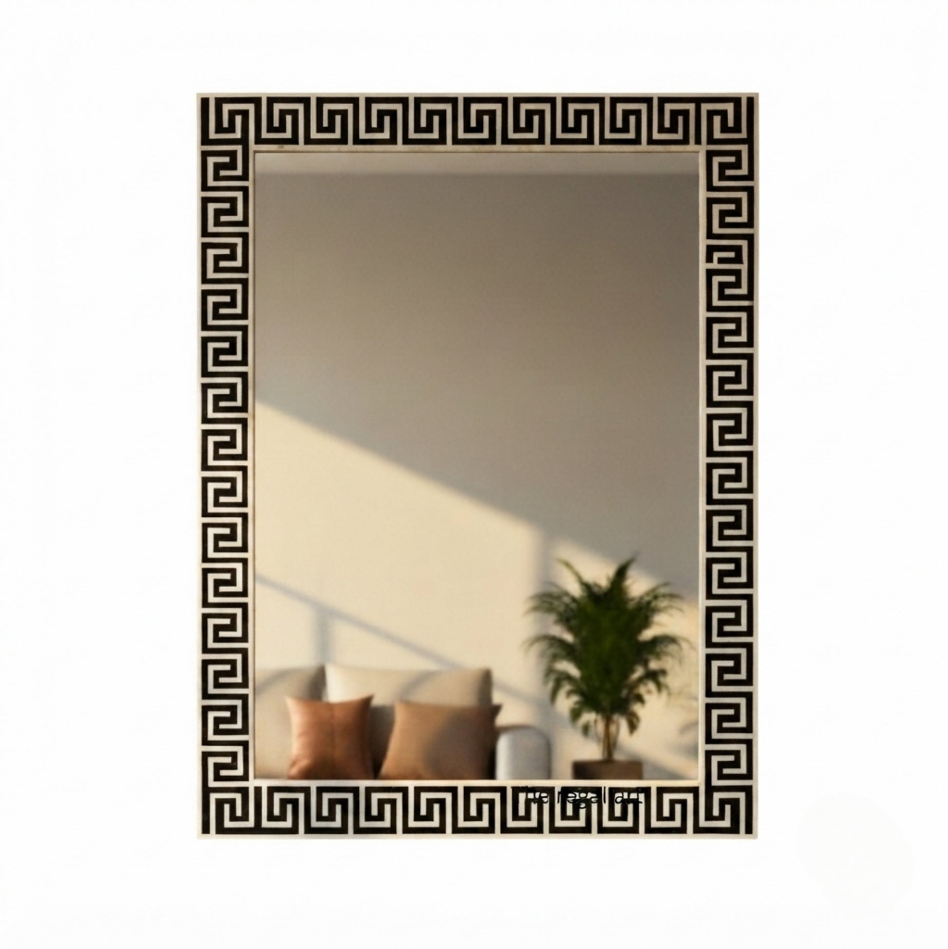 A rectangular wall mirror with a black Greek key pattern border, shown against a plain white background. The mirror reflects a warm-toned interior scene with a sofa, pillows, and a potted plant.