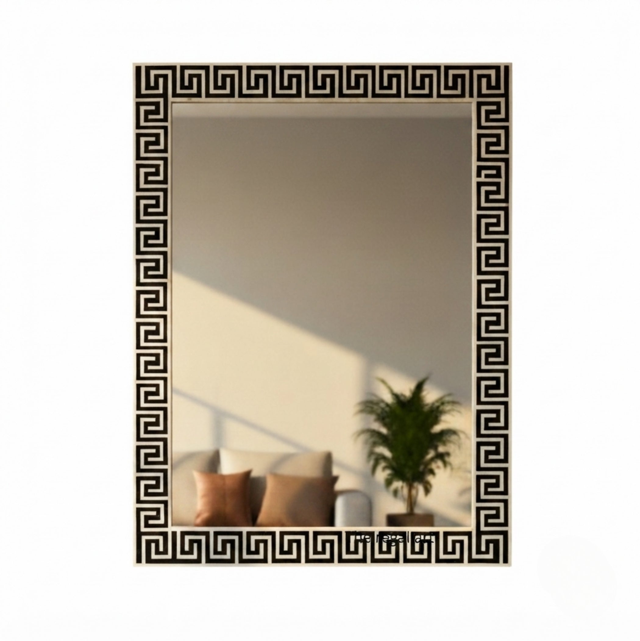 A rectangular wall mirror with a black Greek key pattern border, shown against a plain white background. The mirror reflects a warm-toned interior scene with a sofa, pillows, and a potted plant.