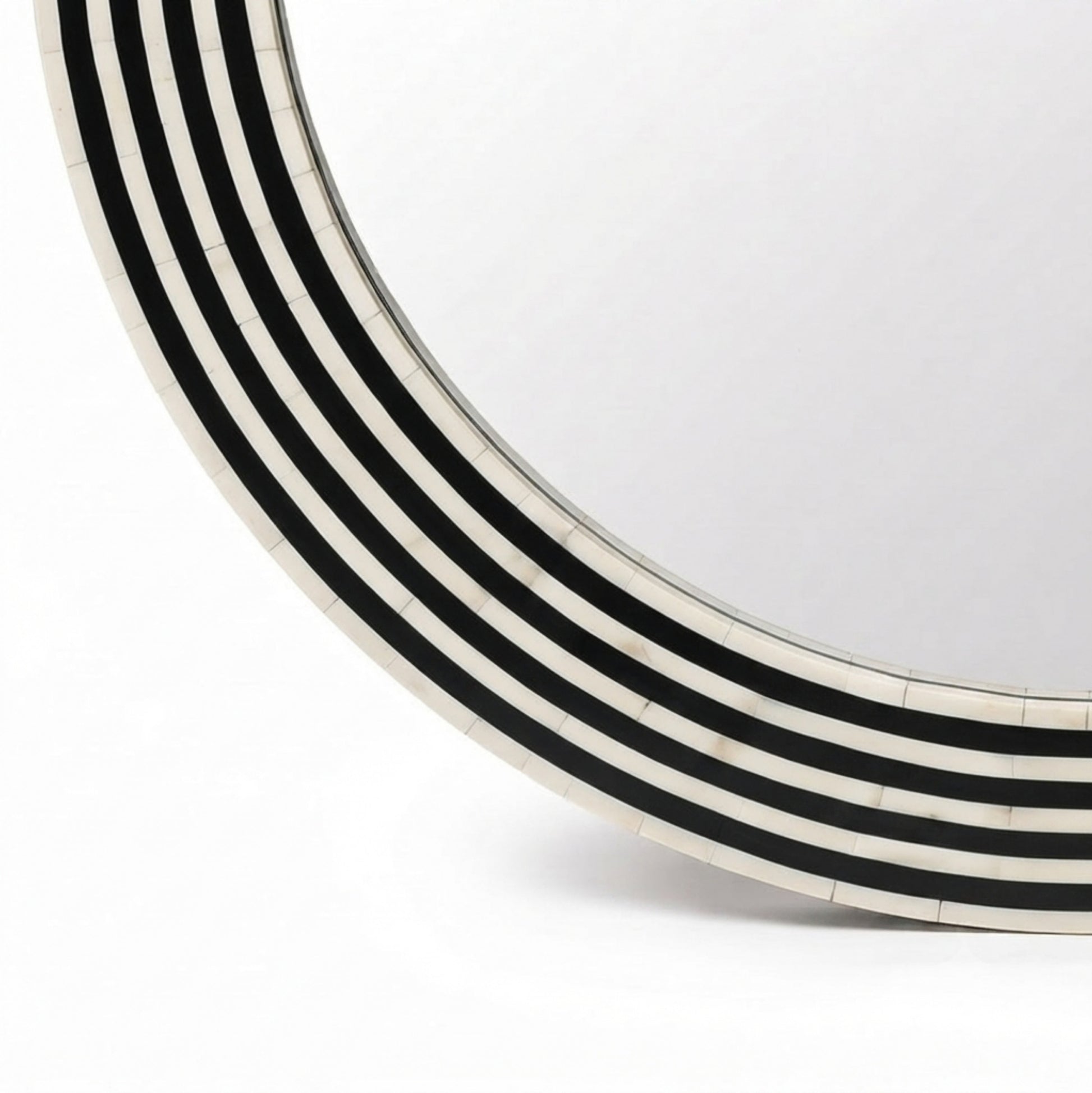 A close-up of a round mirror with a curved frame made of alternating black and off-white inlay stripes, set against a plain white background.
