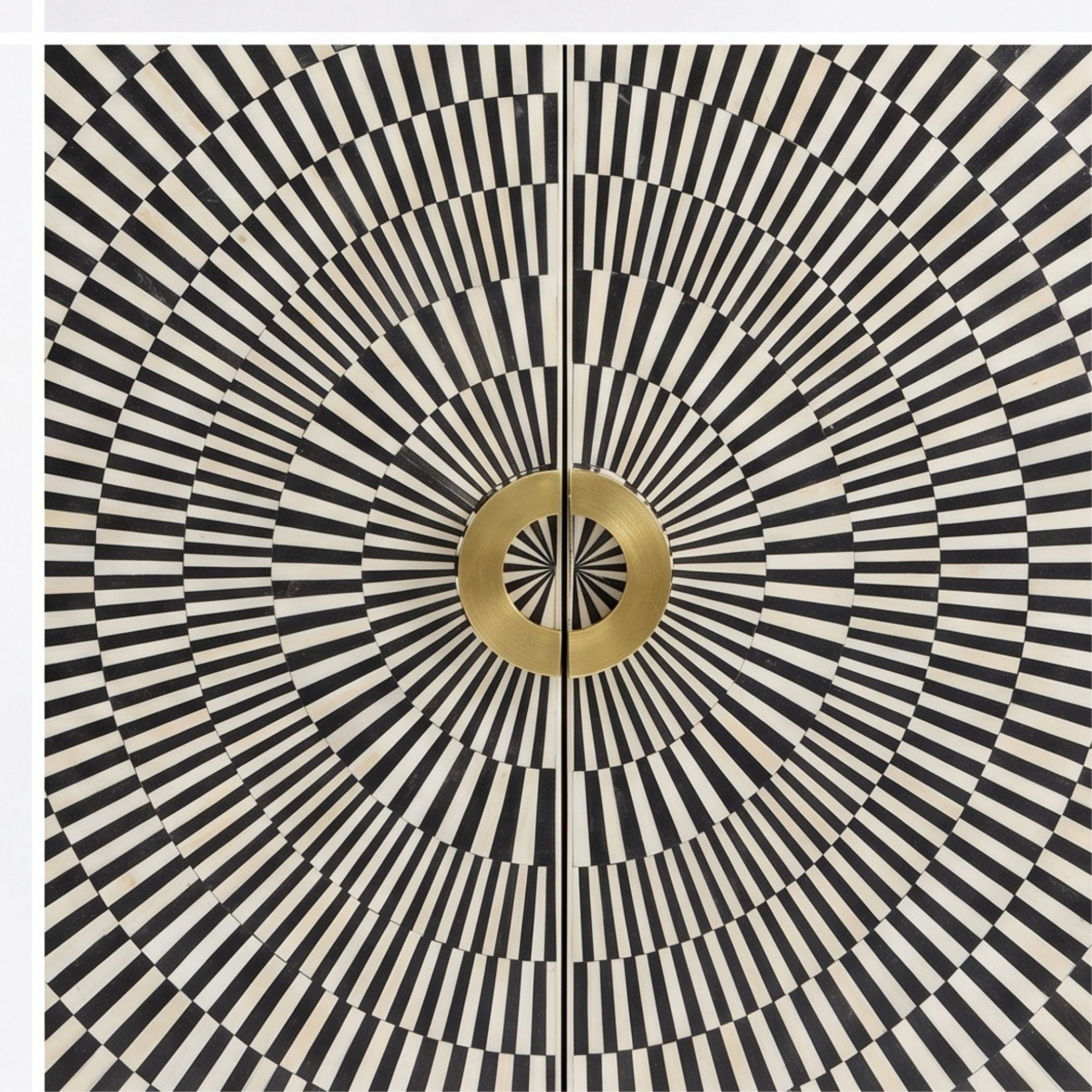 A square decorative panel or door featuring a bold black and off-white radial stripe pattern with concentric circles and a central metallic gold circular medallion.