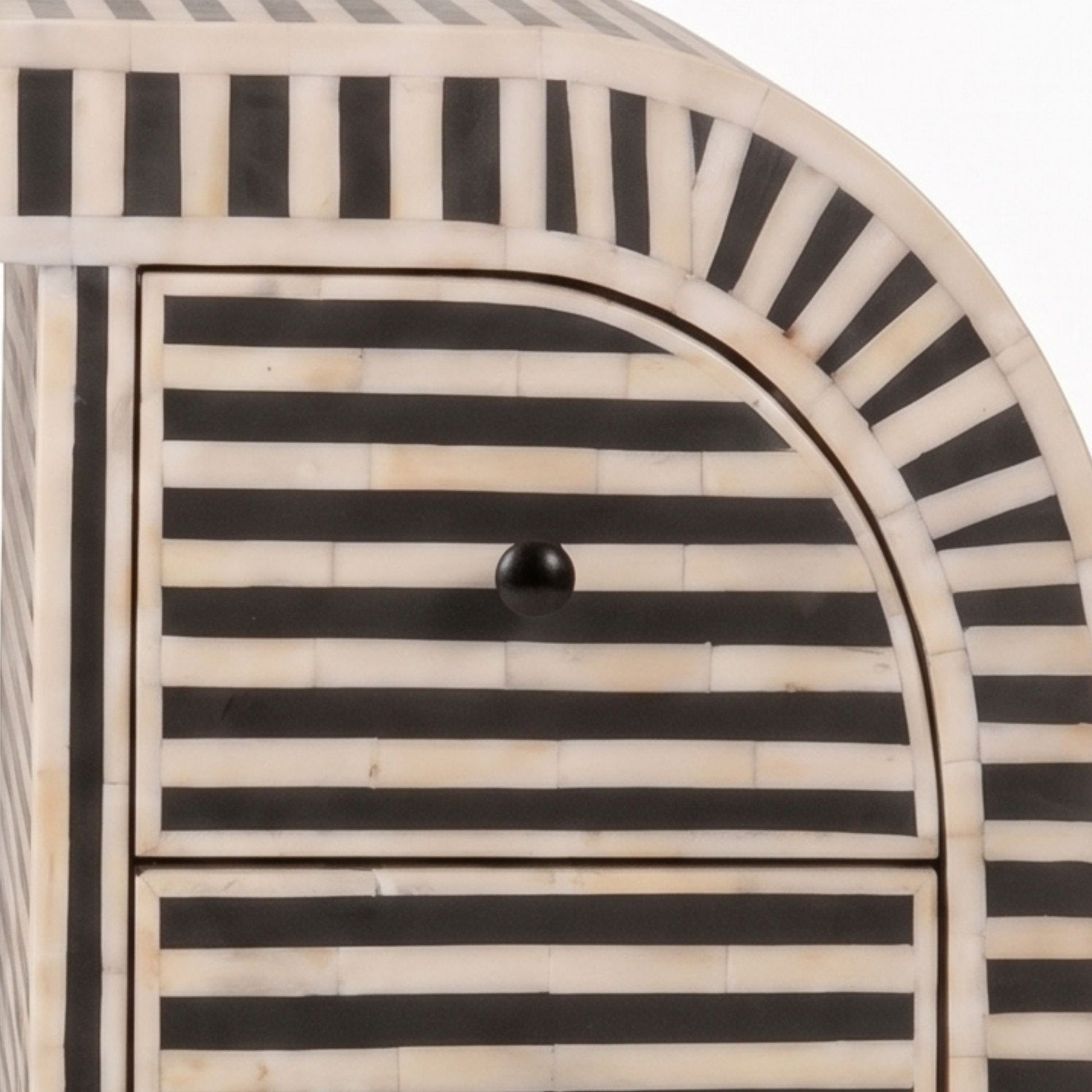 Close-up of a striped furniture piece, likely a cabinet or chest, featuring alternating black and cream bone-in-laminate horizontal stripes with a small black round knob on the front drawer.