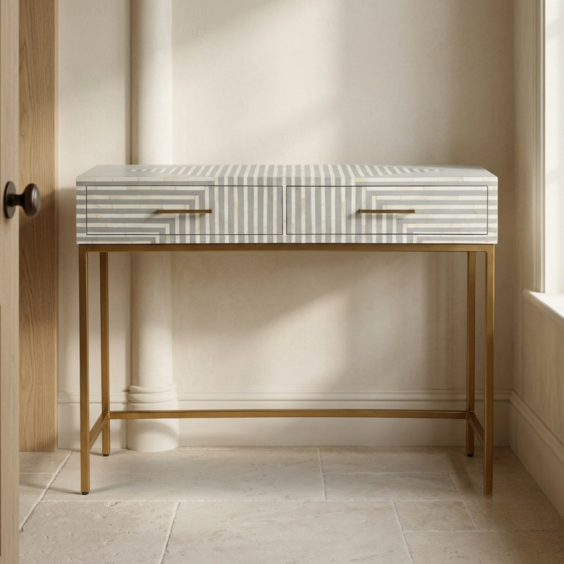 A modern console table with striped and geometric drawer fronts, a white marble top, and a gold metal frame, styled in a contemporary room next to a cream armchair.