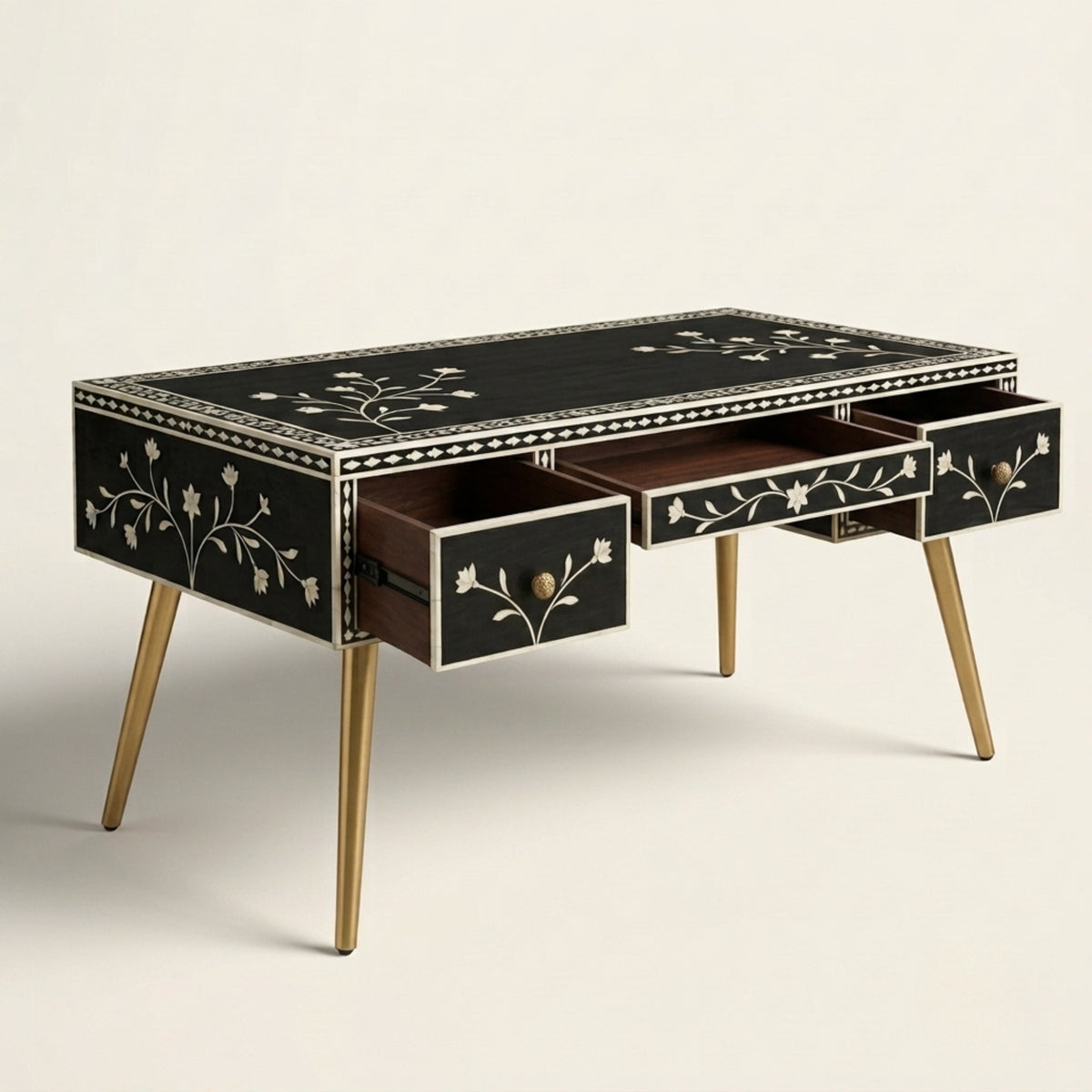 A mid-century modern writing desk with a black mother-of-pearl inlay top and drawer fronts, featuring delicate floral vine patterns, exposed wood drawer interiors, and tapered gold-finished legs.