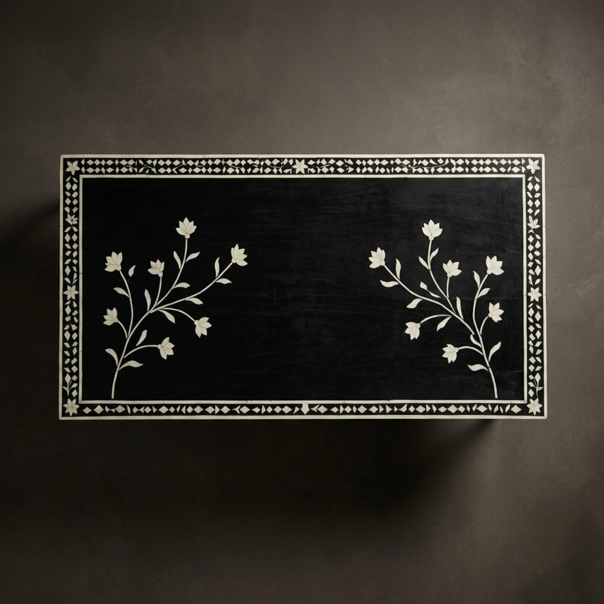 A rectangular black wooden chest or box with intricate white mother-of-pearl floral inlay designs on the front, set against a dark textured background.