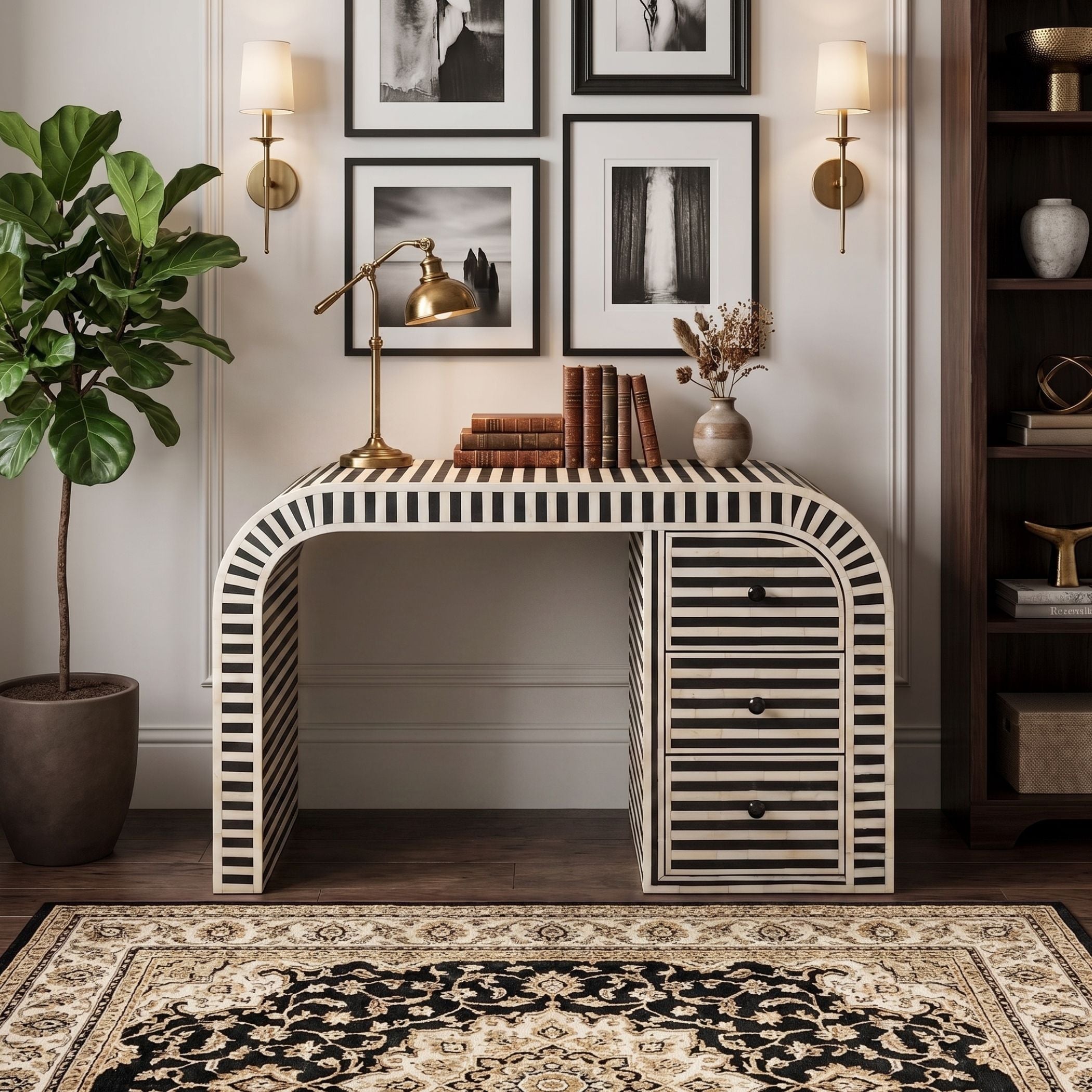 A console table with a black and white striped bone-and-wood frame, styled in a home office setting with books, a brass desk lamp, wall sconces, framed art, a potted plant, and a patterned rug.
