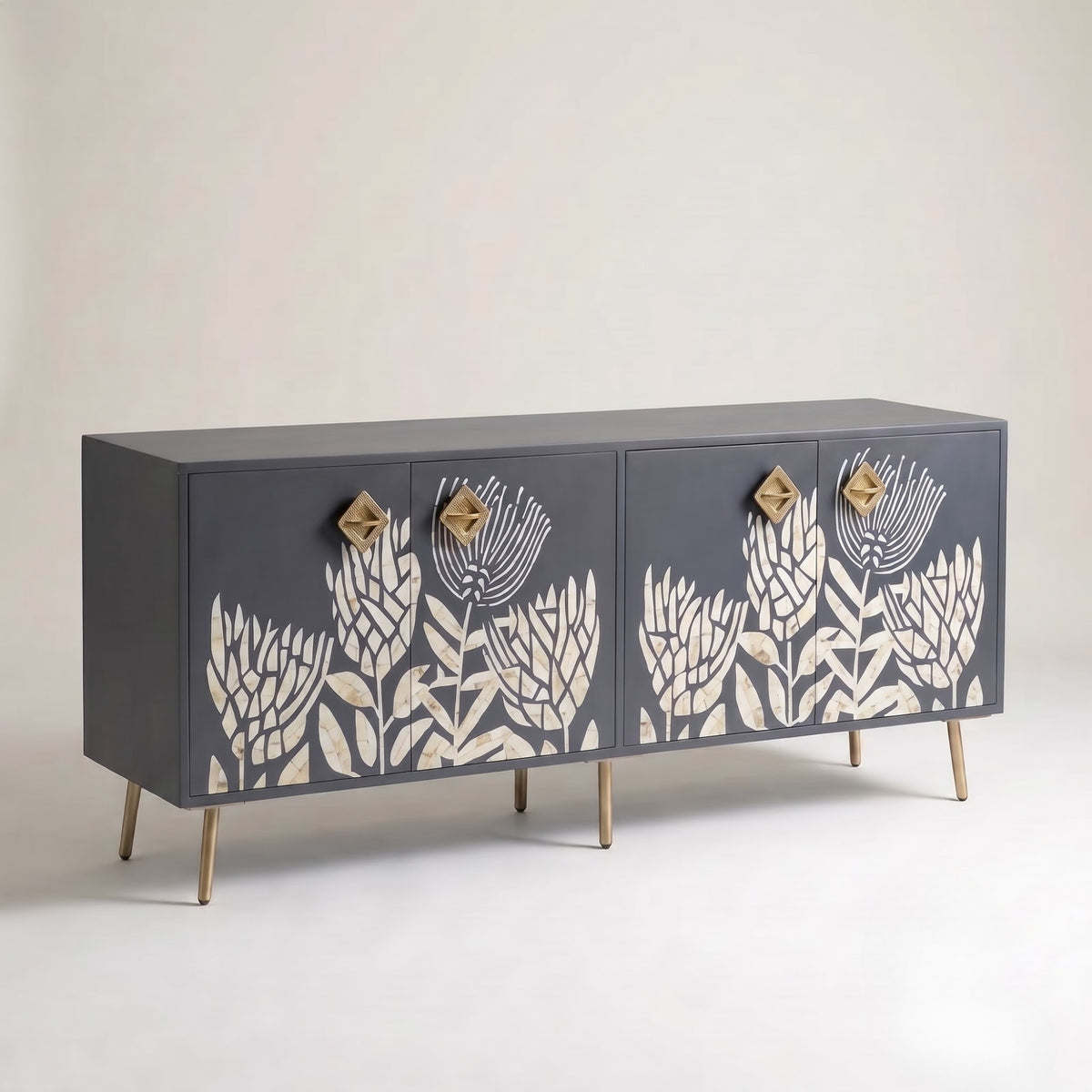 A mid-century modern sideboard featuring a dark charcoal gray finish with cream floral inlays and gold-toned geometric drawer pulls and legs, set against a neutral light gray background.