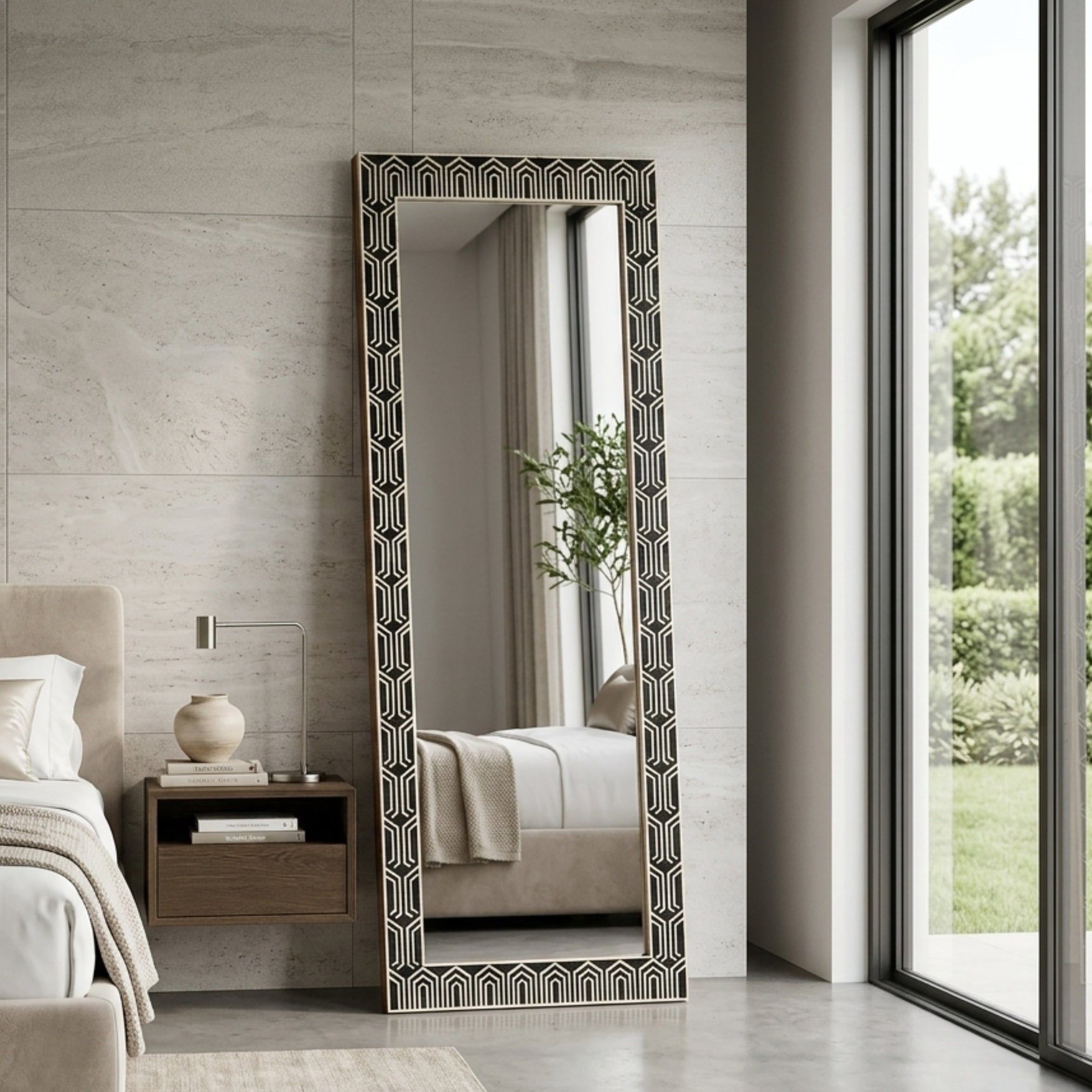 A tall floor mirror with an ornate black and white geometric patterned frame, standing in a modern bedroom next to a bed and window.