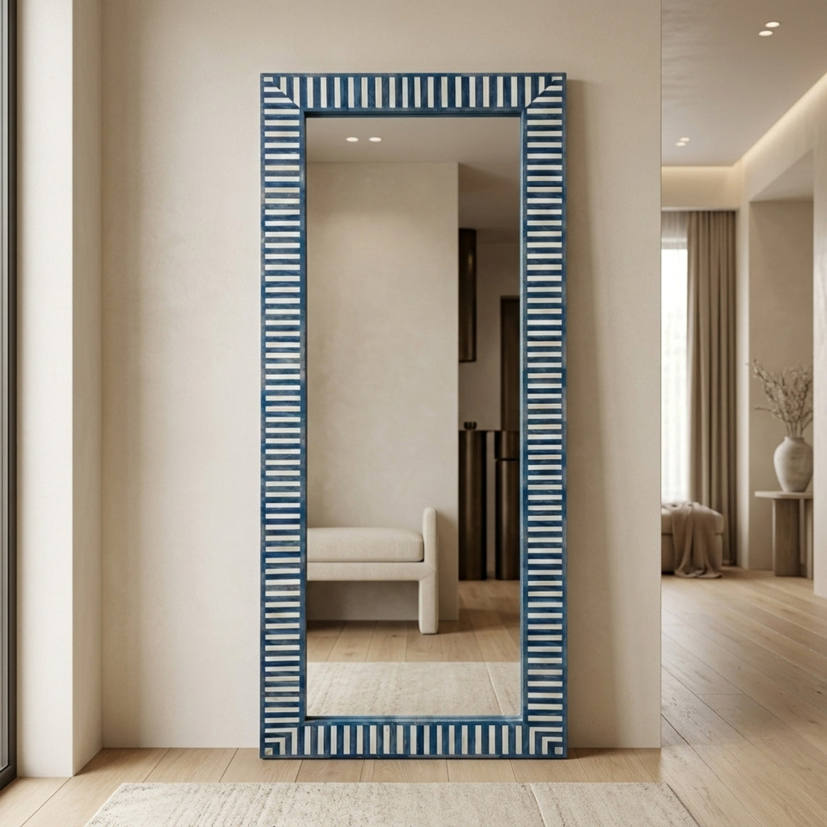 A tall rectangular wall mirror with a blue and white striped frame, standing on a light rug in a modern beige-toned interior hallway.
