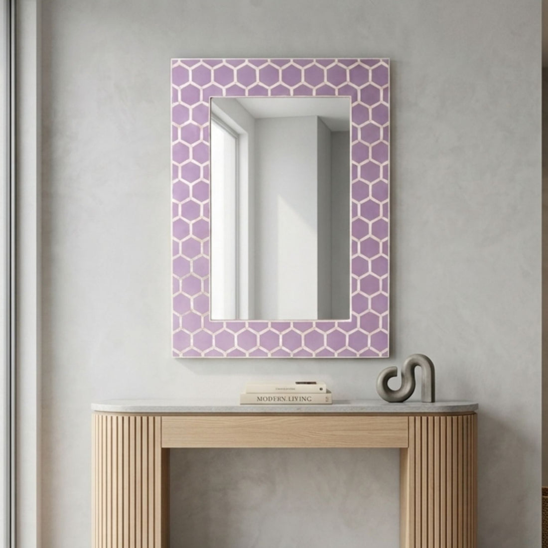 A rectangular wall mirror with a lavender and white geometric honeycomb patterned frame, mounted on a textured light gray wall above a light wood console table.