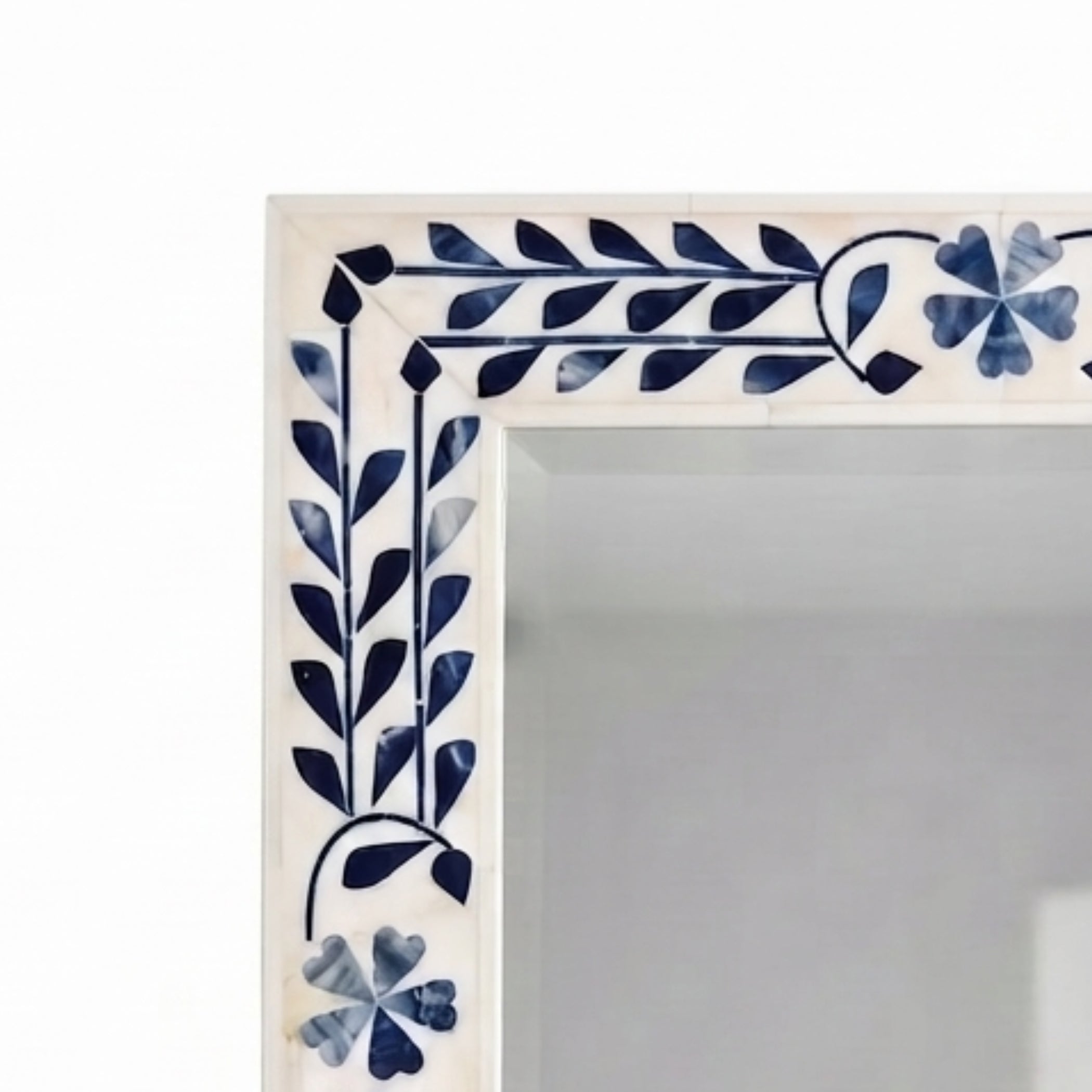 A close-up of a decorative rectangular frame corner with a white background and navy blue floral and leaf inlay pattern.