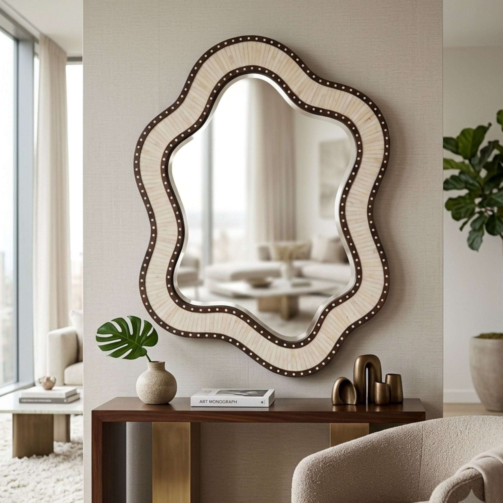 An ornate scalloped wall mirror with a cream and brown wavy frame and dark nailhead trim, displayed in a modern, neutral-toned living room above a wooden console table.