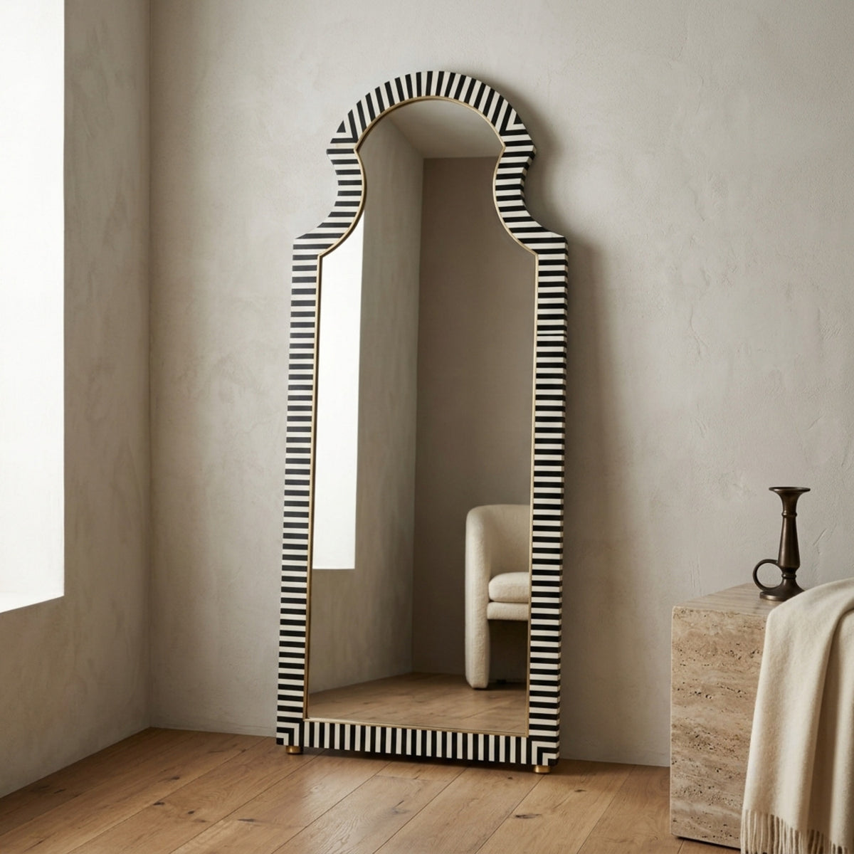 Arched full-length floor mirror with a black and white striped border, standing in a neutral-toned room with wood flooring.