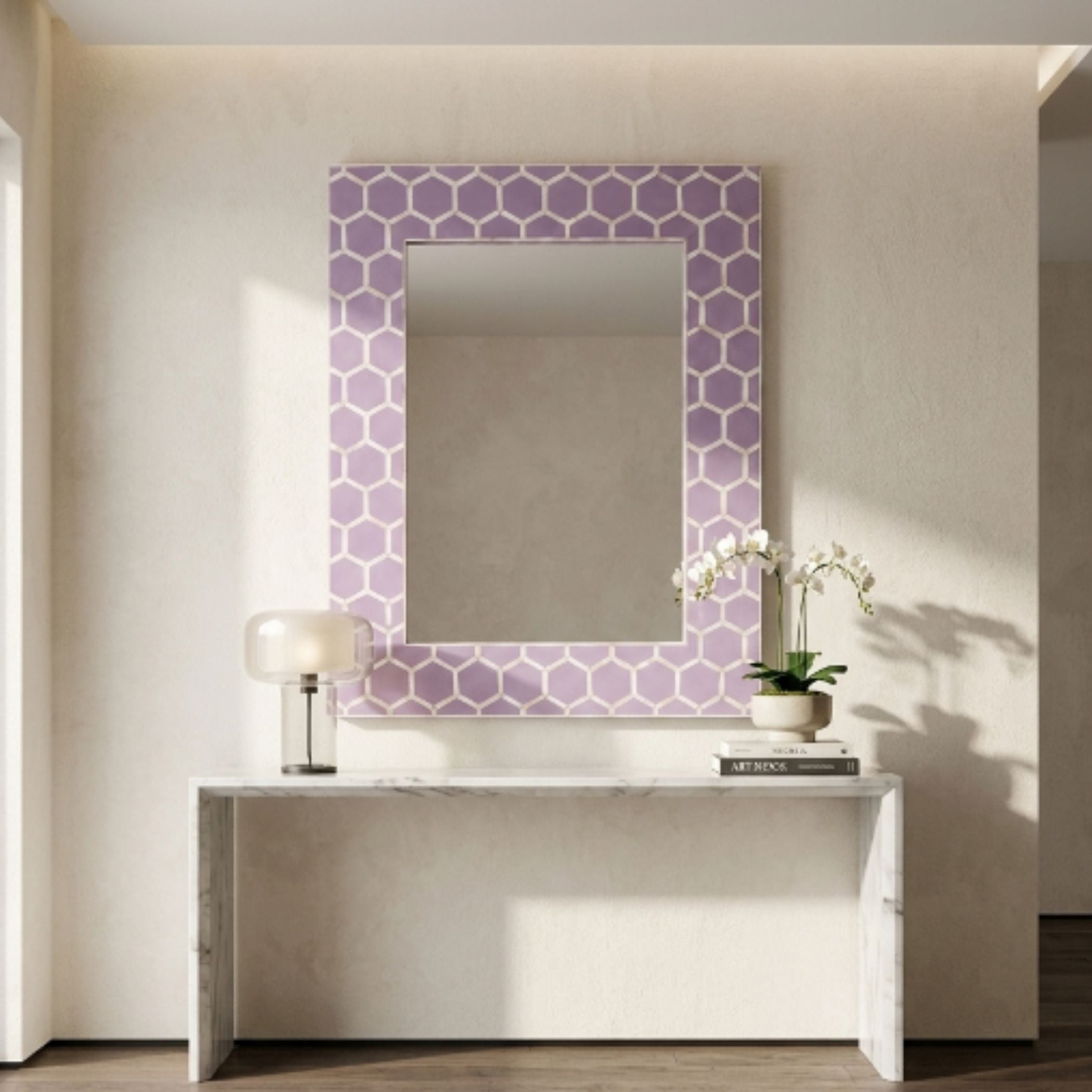 A rectangular wall mirror with a lavender and white geometric honeycomb patterned frame, styled on a white console table against a beige wall.