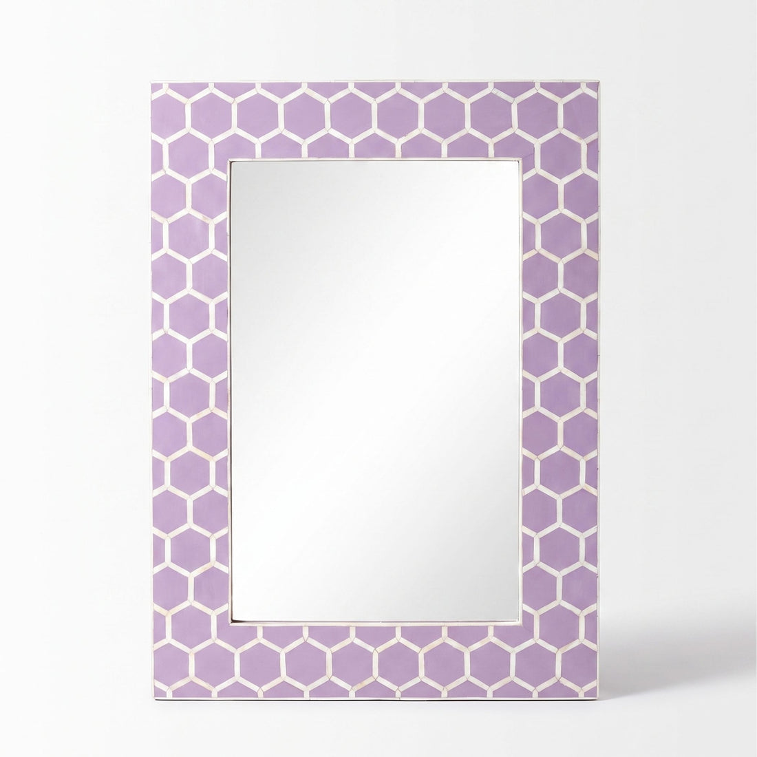 A rectangular wall mirror with a lavender and white geometric honeycomb patterned frame, mounted on a textured light gray wall above a light wood console table.