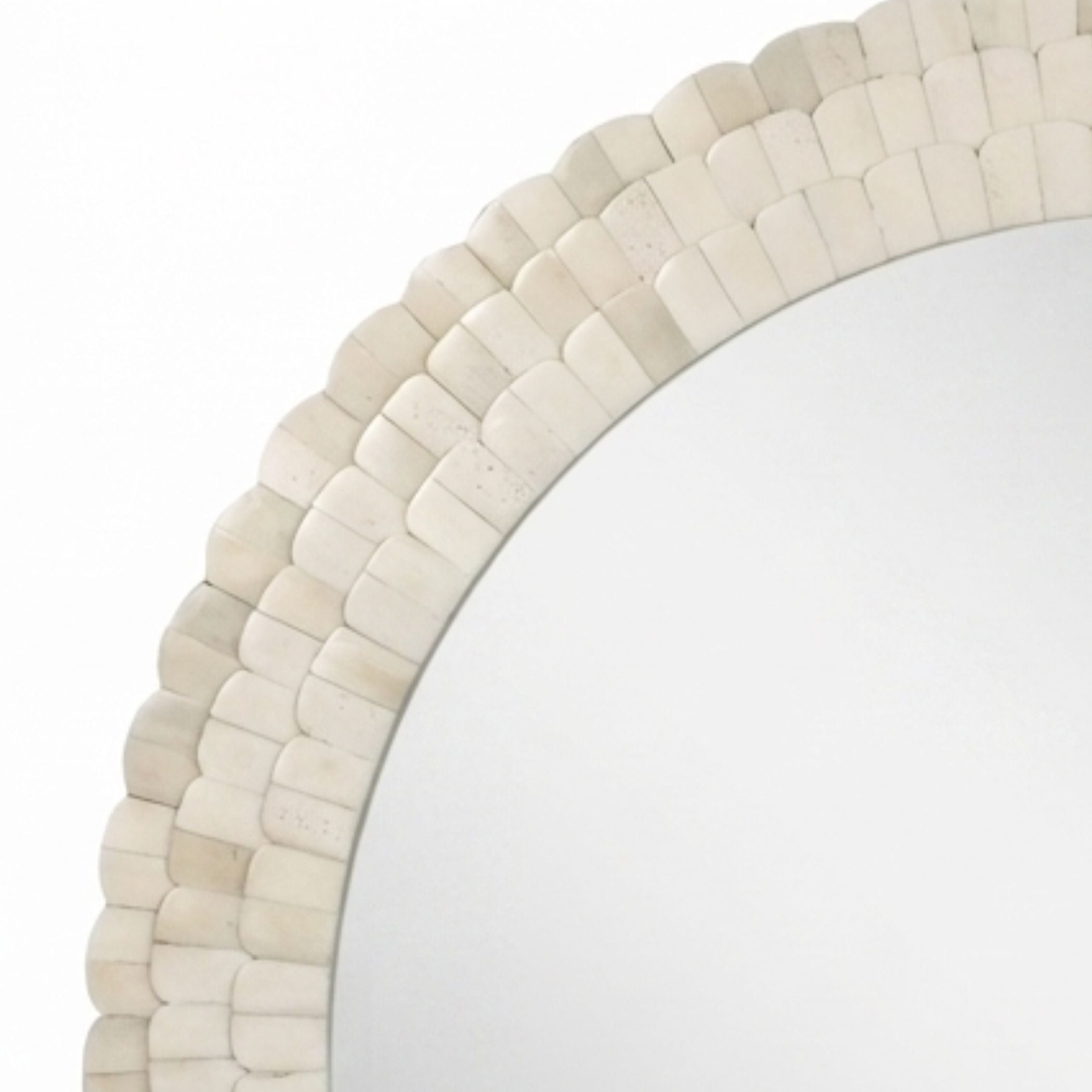 A close-up of a round mirror with a decorative scalloped frame made of small overlapping shell-like pieces in an off-white or cream tone, shown against a white background.