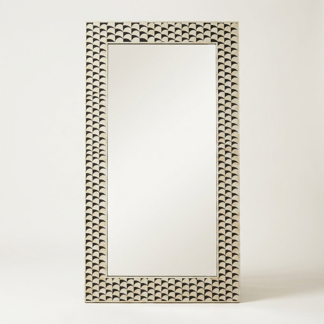 A rectangular wall mirror with an ornate, textured frame featuring a repeating scalloped shell-like pattern in a warm beige and dark brown tone, set against a plain off-white background.